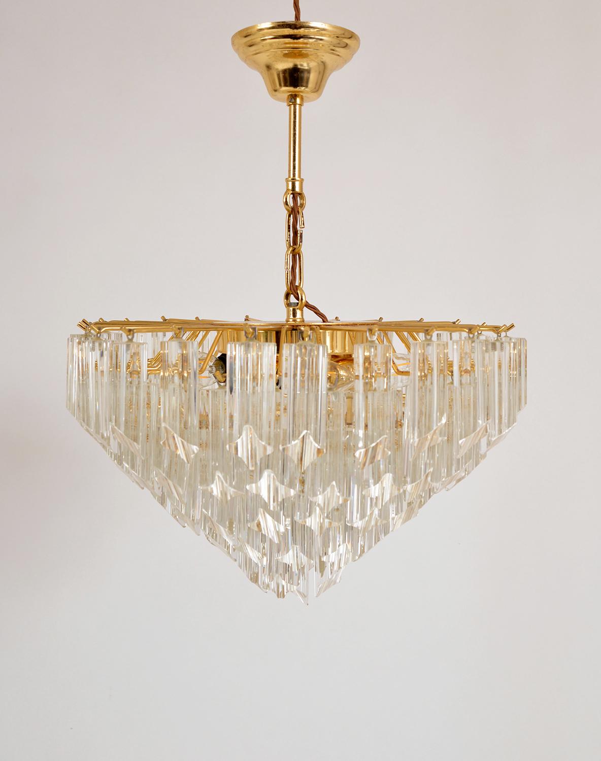 Stunning 1970s Italian chandelier by Novaresi Luce Milano, with clear Murano glass cut drops in the Quadriedri technique, arranged in descending layers from a 24 carat gilded brass frame with four bulbs. 
There are a couple of small nibbles on a
