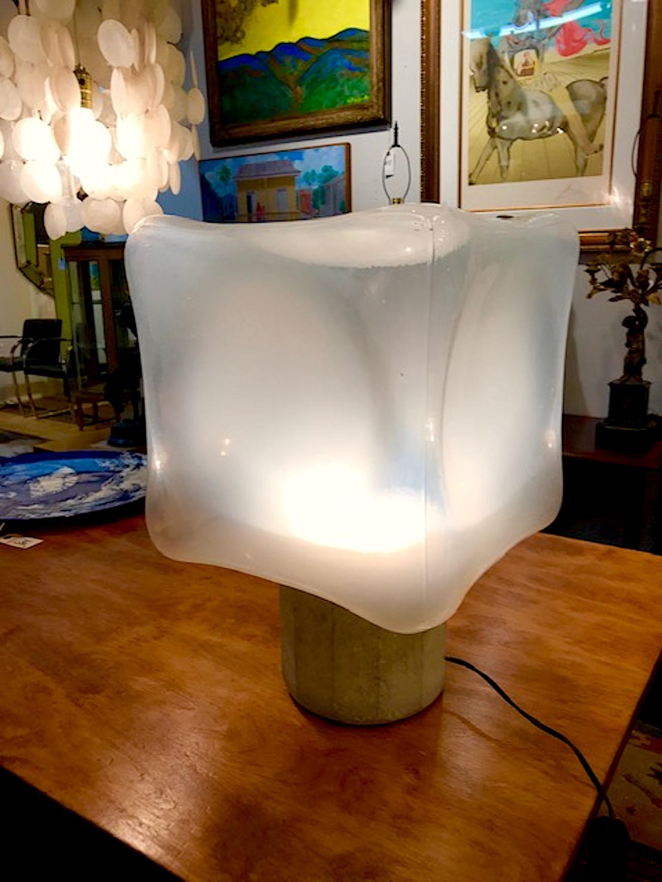 A wonderful and sculptural table lamp by Italian lighting company Leucos, circa 1970. A large Murano hand blown cube glass shade in clear to white glass sits atop a faceted raw stone base. The base has a standard socket set inside an aluminum dish.