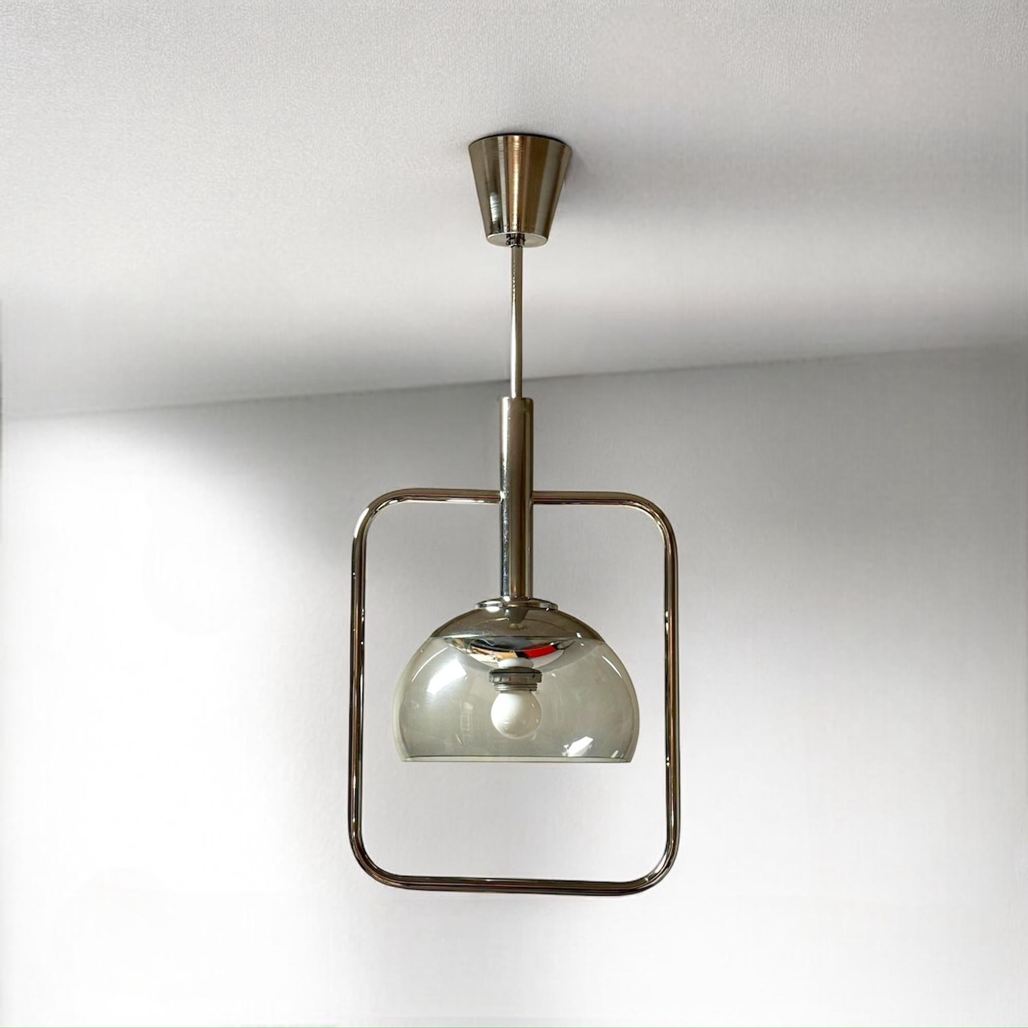 Incredibile lampada a sospensione degli anni '70, caratterizzata da un diffusore in plexiglass affumicato che crea un bagliore caldo e suggestivo pur mantenendo un'estetica elegante e futuristica. La struttura in metallo cromato, compresi il fusto e
