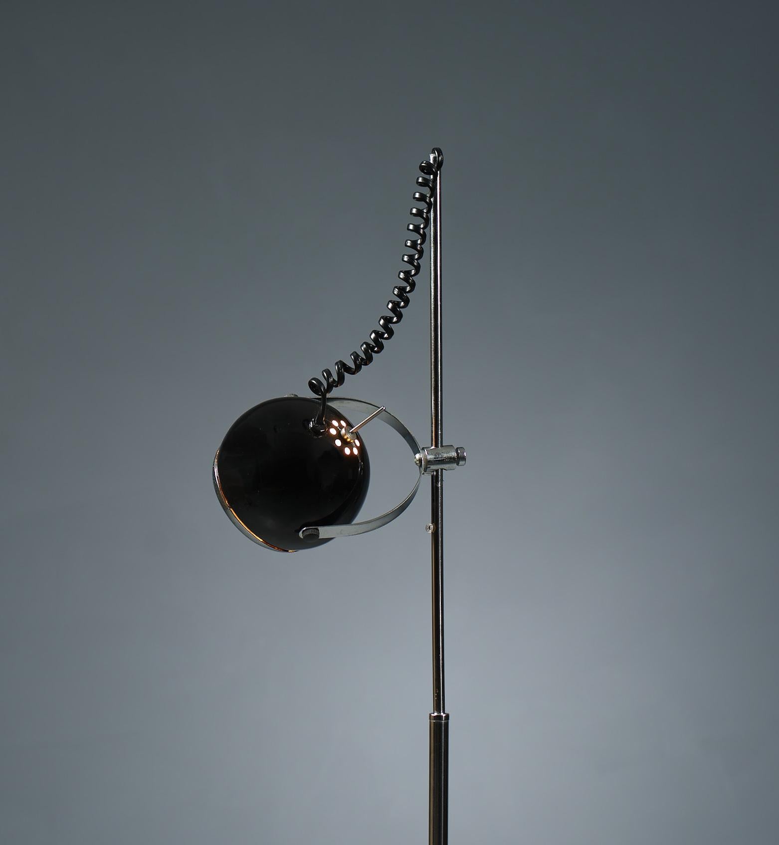 Vintage floor lamp from the 1970s. Crafted in Italy, it boasts a sleek chrome steel construction complemented by black lacquered accents. The adjustable spherical diffuser offers omnidirectional lighting, while its height can be tailored to suit