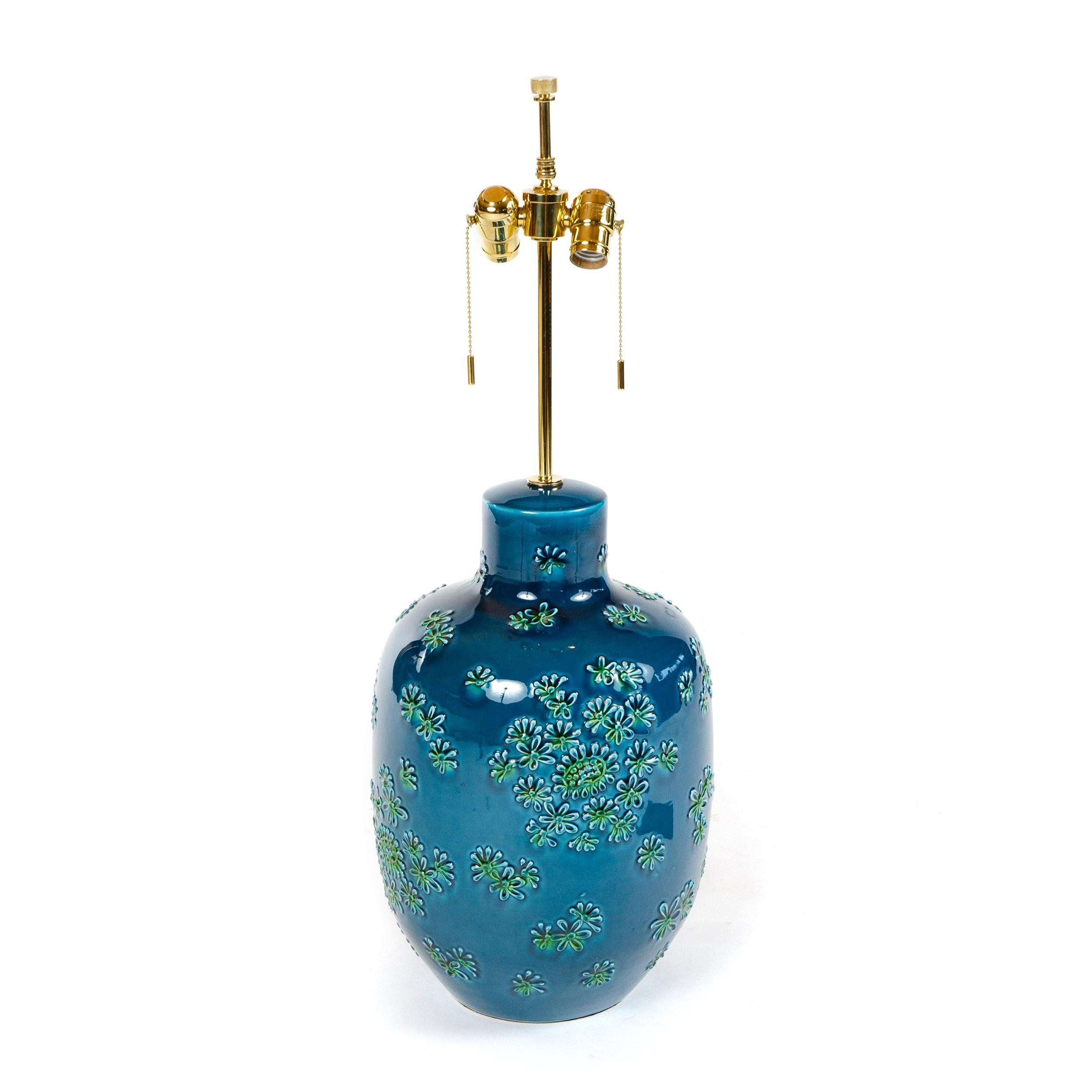 A robust ceramic table lamp with high gloss turquoise glaze and a teal glazed floral motif in relief.