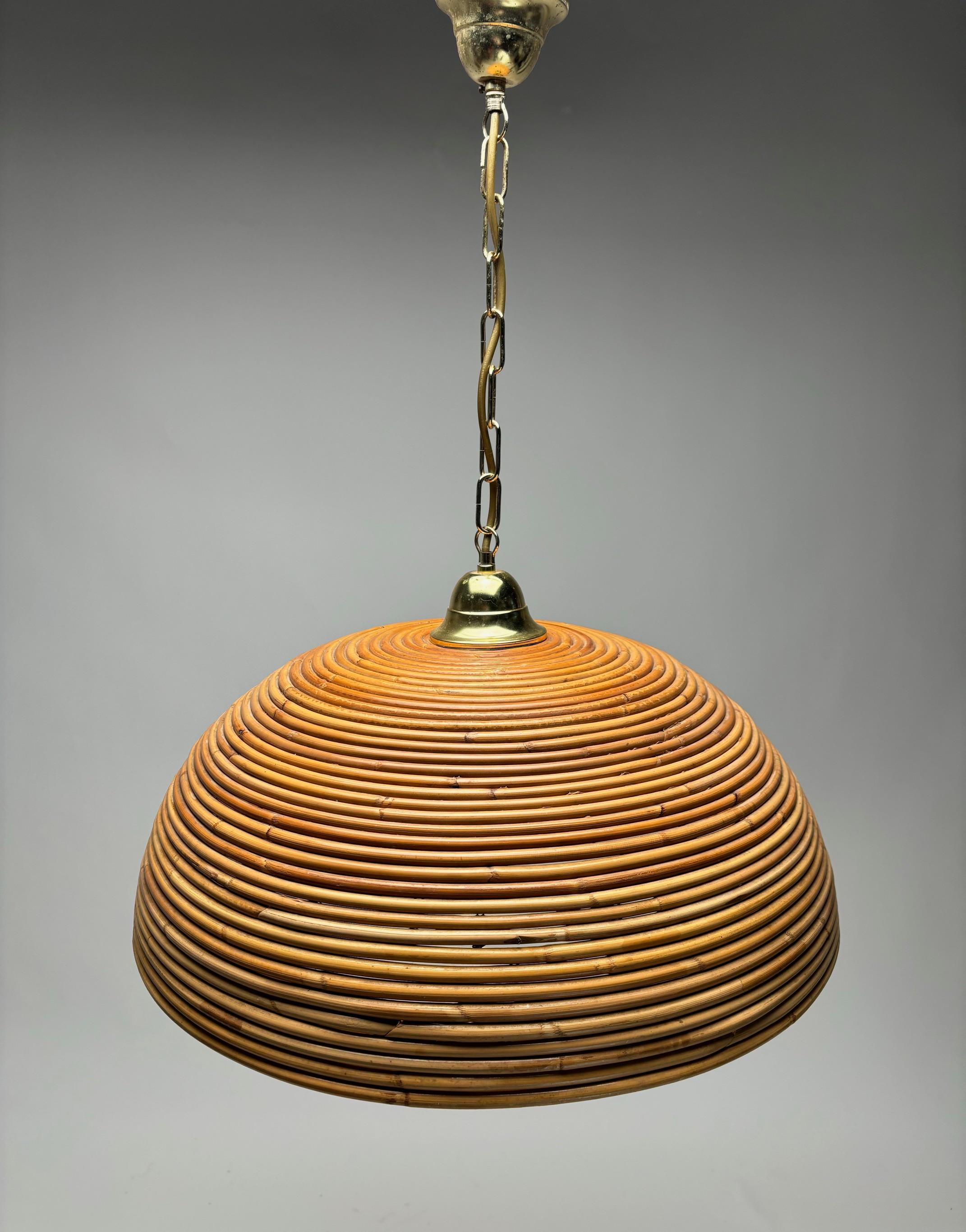 Eyecatching Italian 1960s handcrafted rattan pendant light with circular design. 
This suspension lamp has a bell shaped lampshade hanging from a gilt brass chain topped and ended by a very nice brass bun. The length of the chain can be shortened