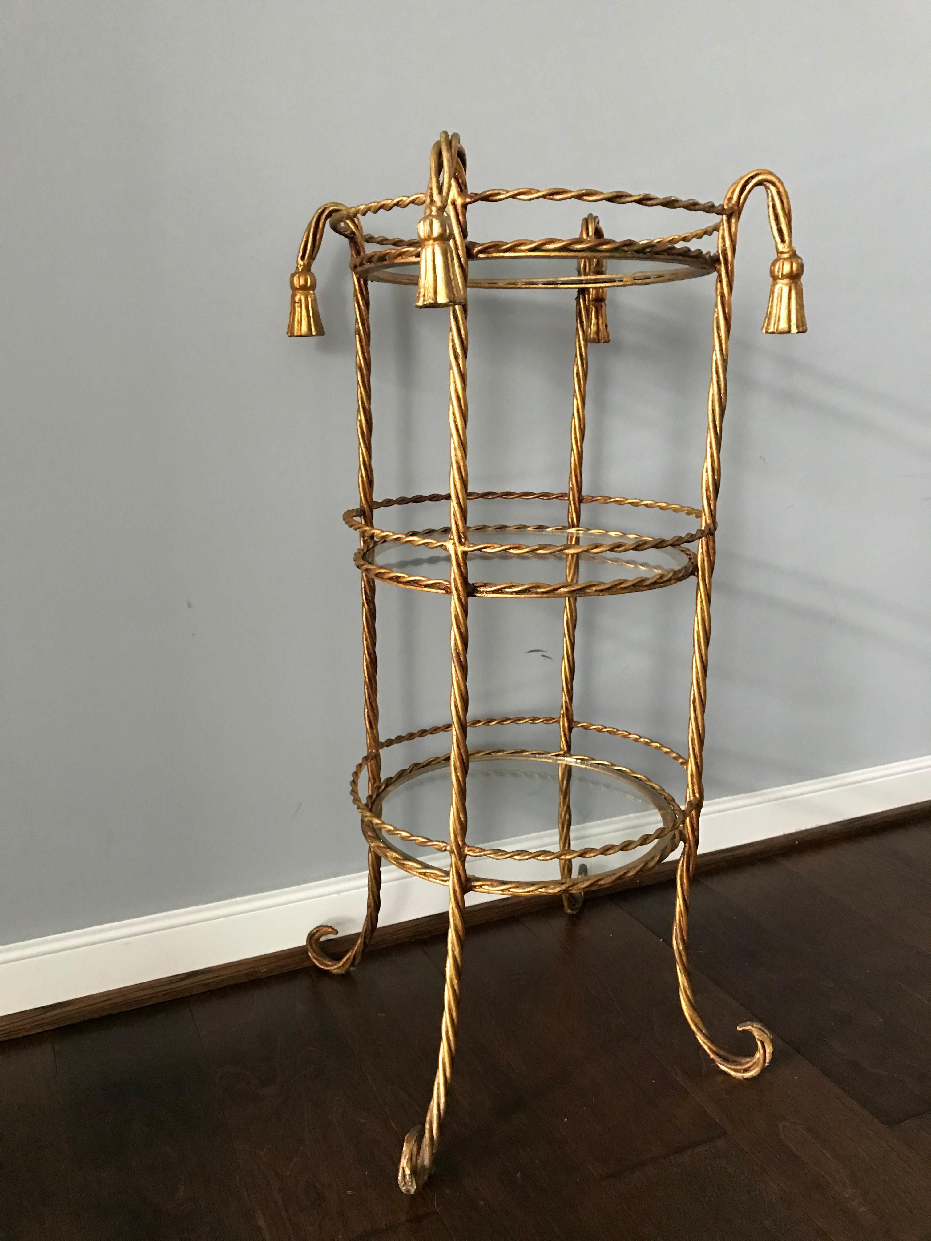 Offered is a gorgeous, 1970s Italian gilt-metal three-tiered table with an allover rope and tassel motif. Three new glass shelves. Measures: 9.25in between shelves.