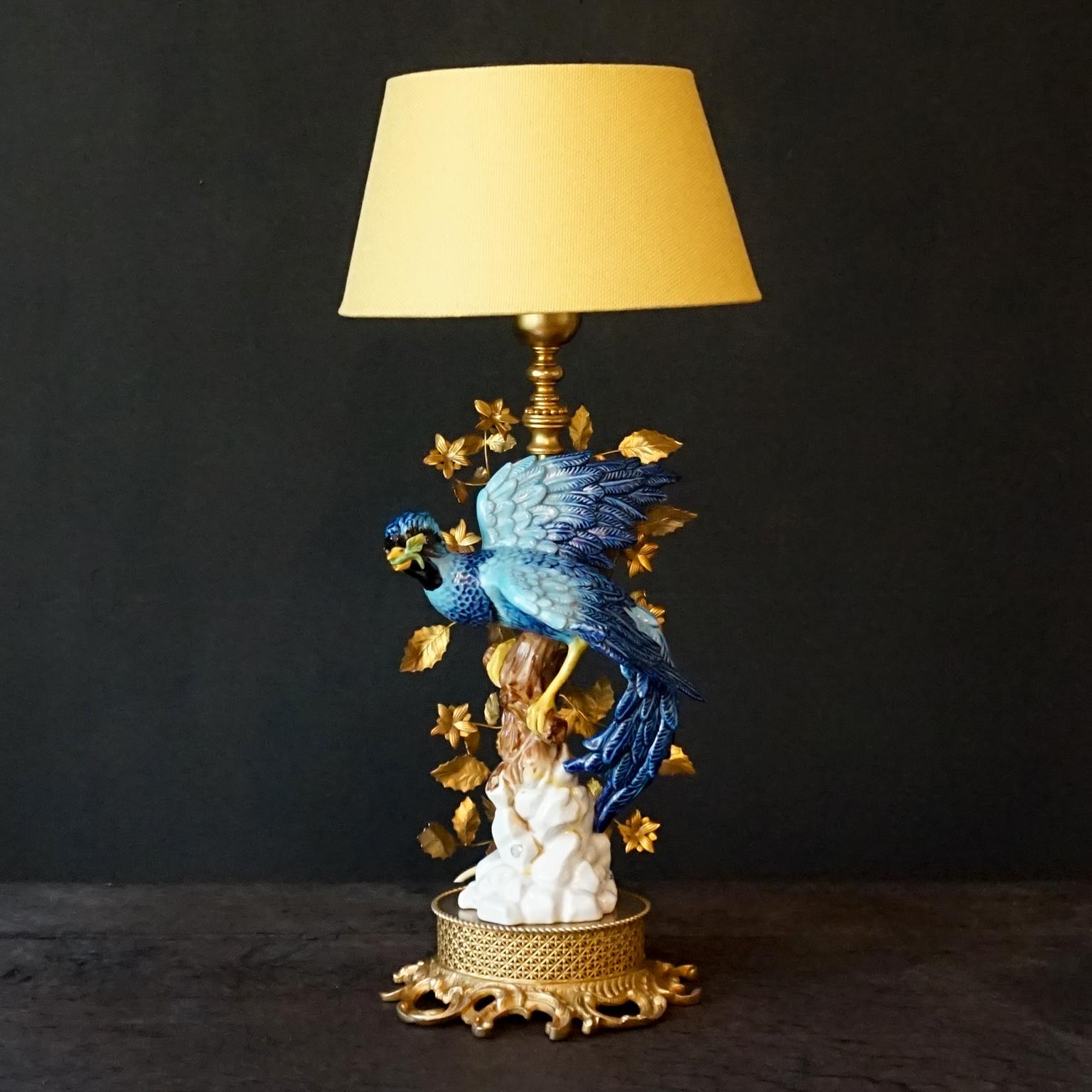 Spektakulär aussehende Tischlampe, die einen handbemalten Porzellanfelsen und einen Ast mit einem auffälligen tropischen blauen Vogel darauf darstellt. Verziert mit Tannenzweigen und Blättern, gekennzeichnet und hergestellt von Giulia Mangani, um