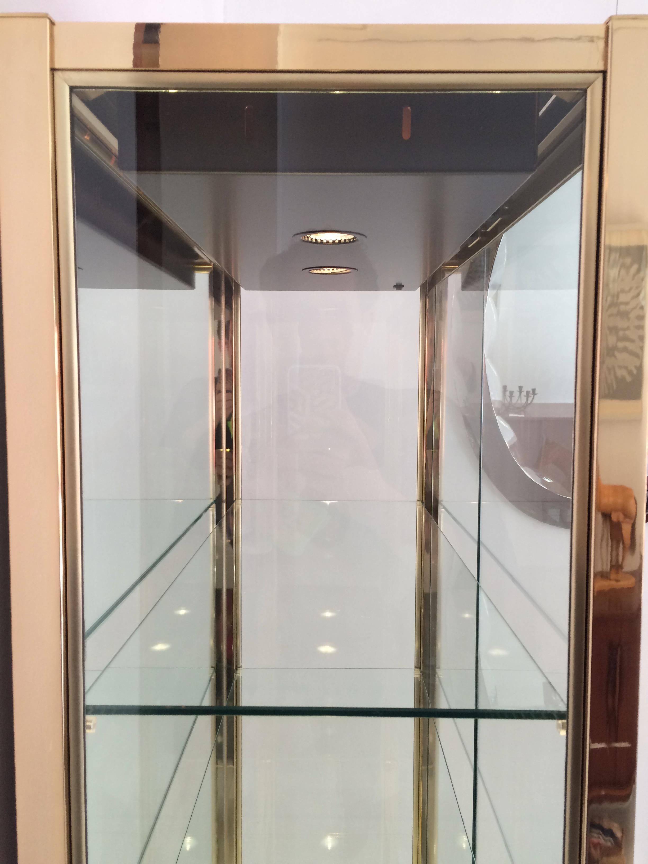 1970s Italian, illuminated, gold-chrome, display cabinet in the style of Renato Zevi.

This striking cabinet has two clear glass doors (non-lockable), glass sides with a mirrored glass back and base shelf.  Three adjustable toughened glass shelves