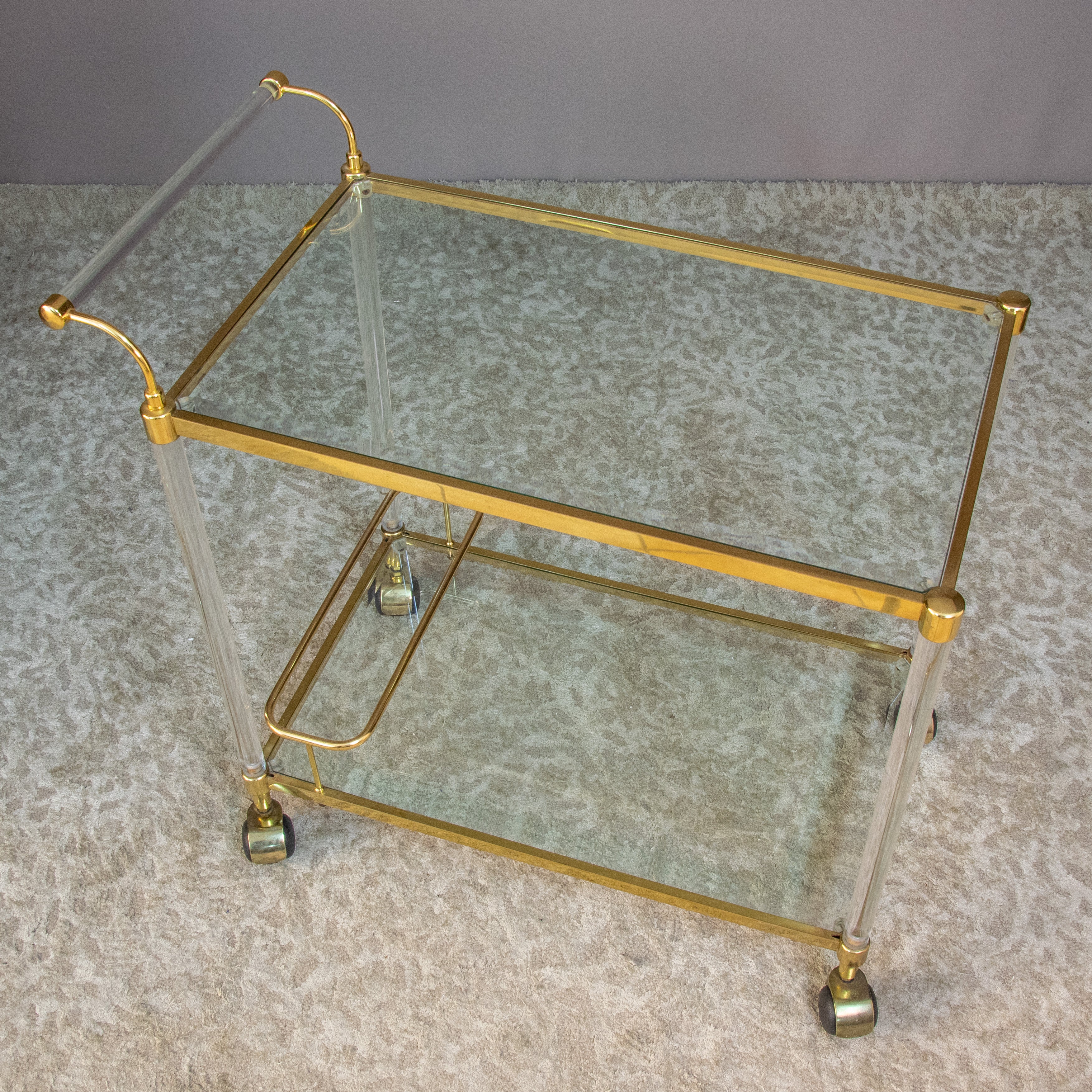 Chariot en laiton doré et lucite des années 1950. 
Le chariot est doté de deux étagères en verre finies en laiton. 
Les bords de l'étagère sont en élégant laiton doré. 
Les quatre roues en caoutchouc sont originales et fonctionnent bien, de sorte