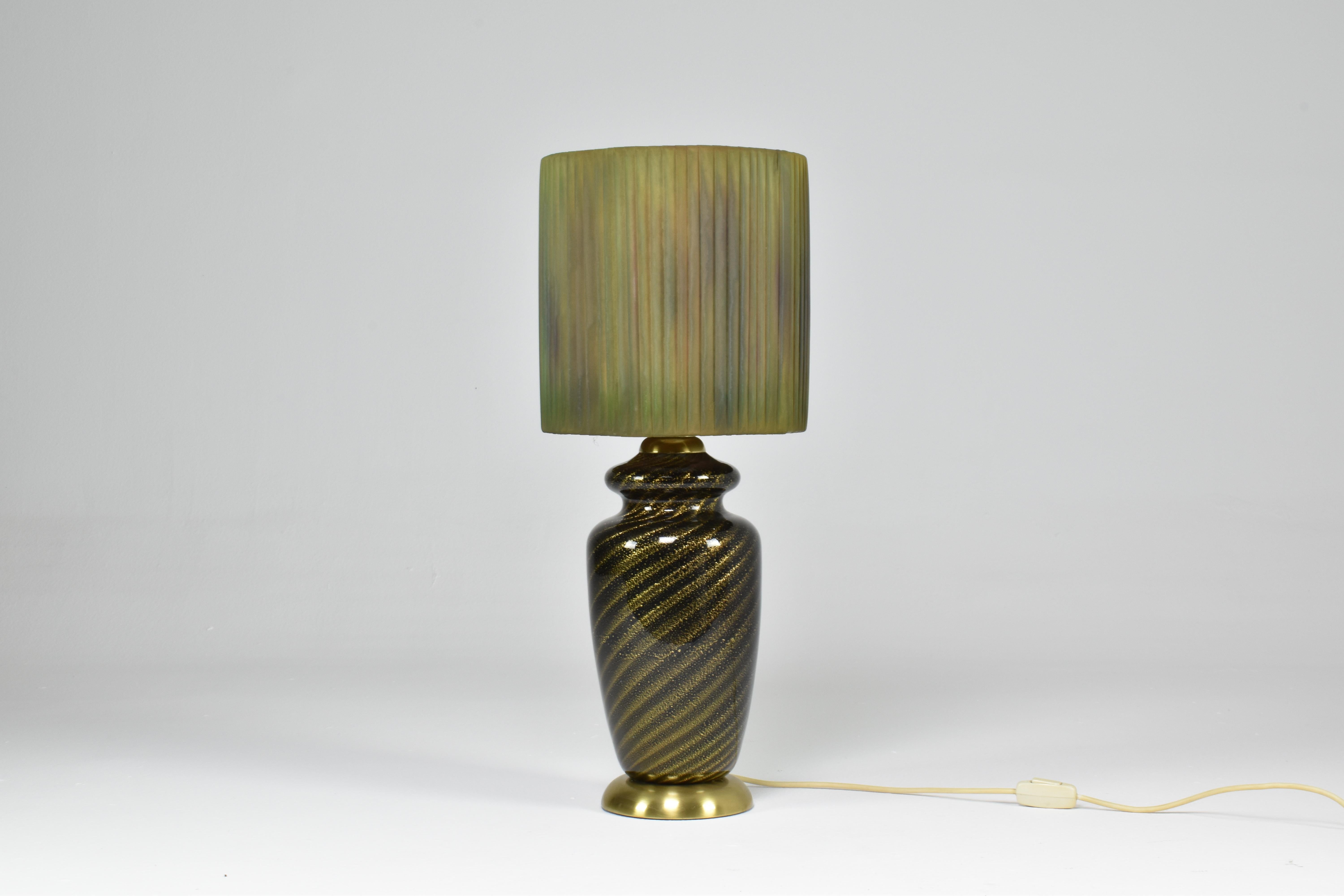 Preciosa lámpara de sobremesa vintage de mediados de siglo, obra del notable diseñador italiano Tommaso Barbi, alrededor de la década de 1970. Esta llamativa pieza de iluminación está elaborada con un cristal verde remolino de Murano con brillos