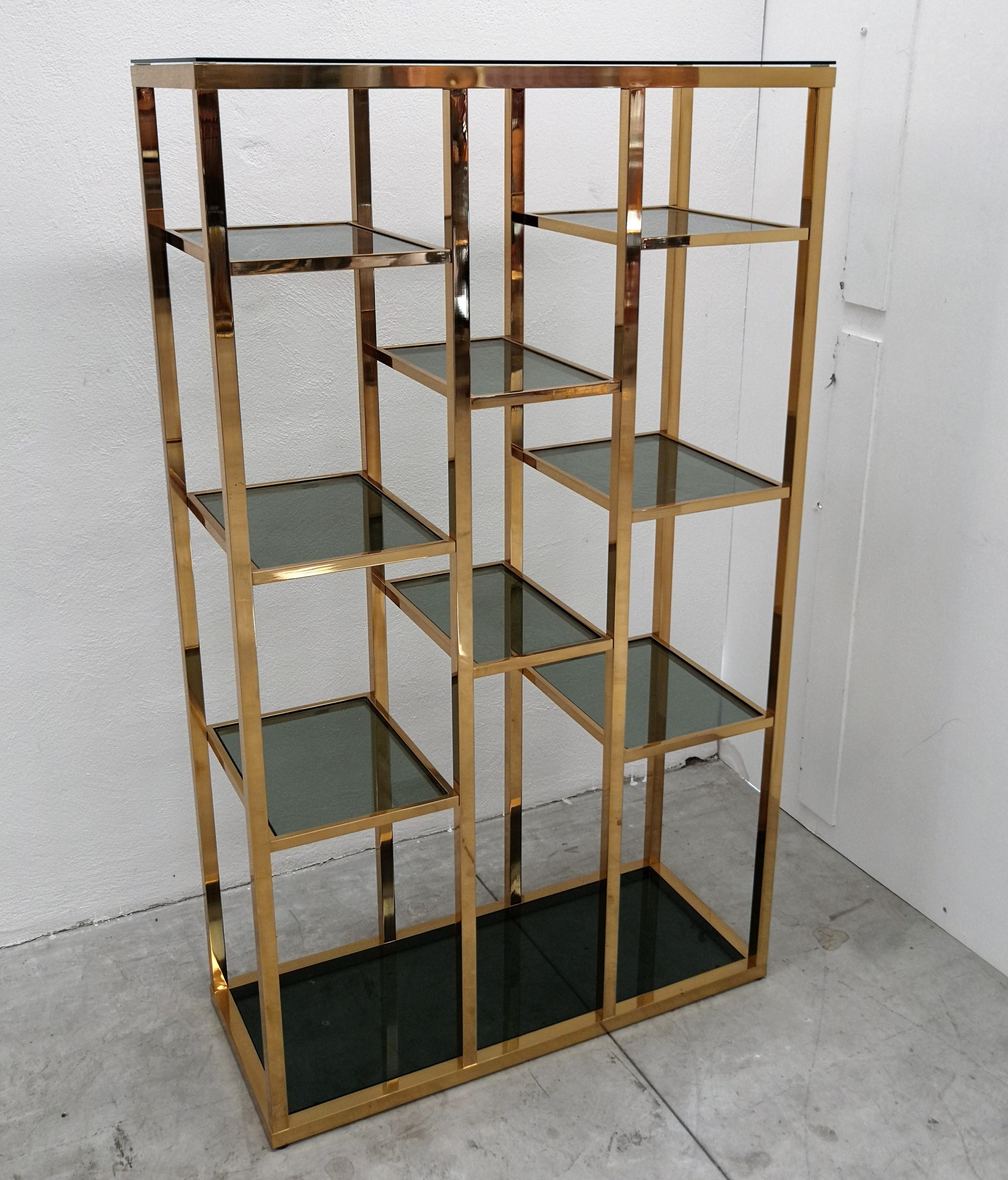 Beautiful and stylish Italian geometric shiny brass étagère, shelving display with top and bottom plus eight central tempered clear green glass inset shelves. A great piece that perfectly adds to every home decor the typical glitz, glamour, and gold