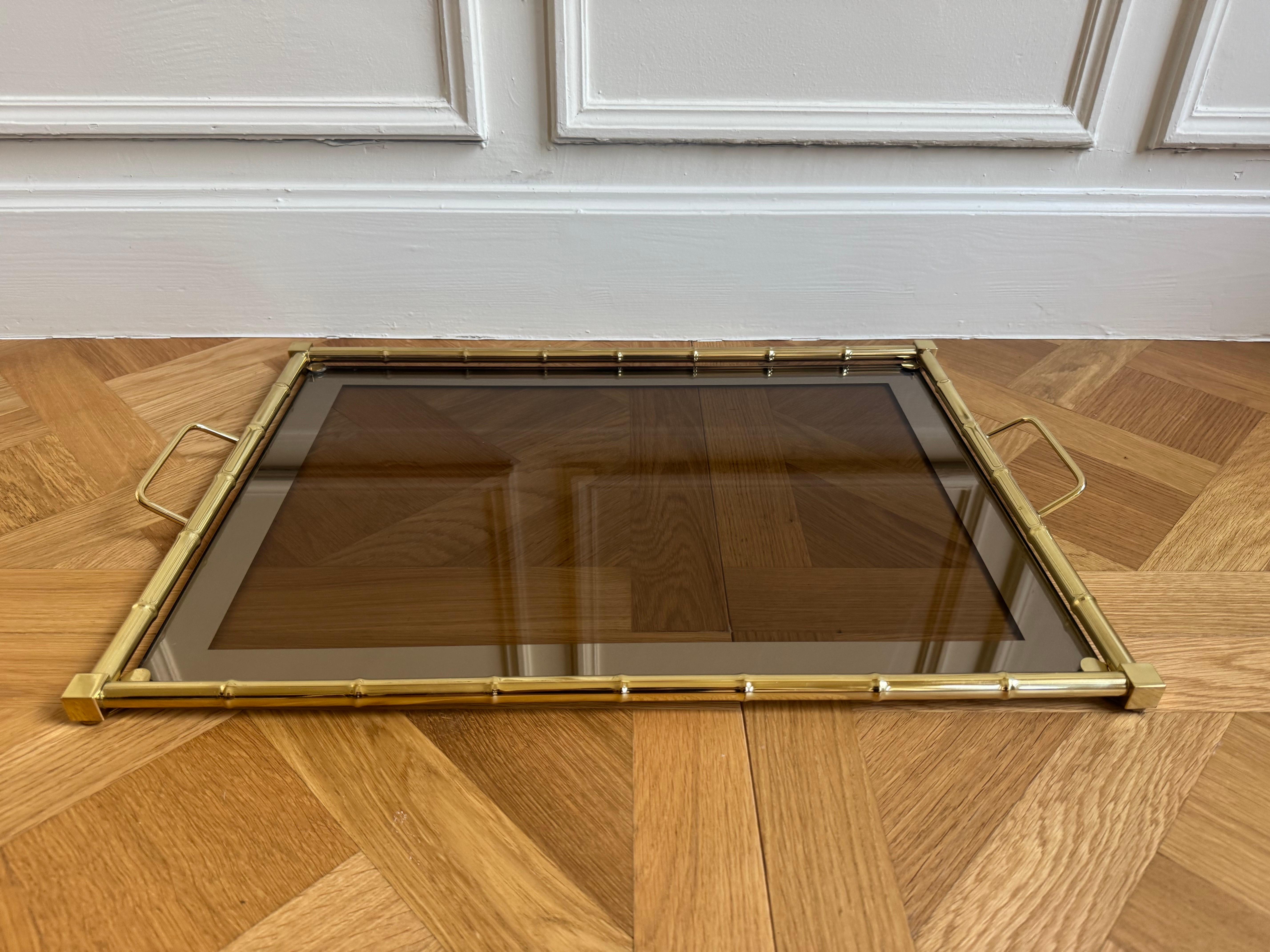 Evocando la elegancia del diseño italiano de los años 70, esta bandeja de servir vintage está elaborada con un marco de imitación de bambú en metal con acabado dorado y presenta una elegante superficie de cristal ahumado. La combinación de
