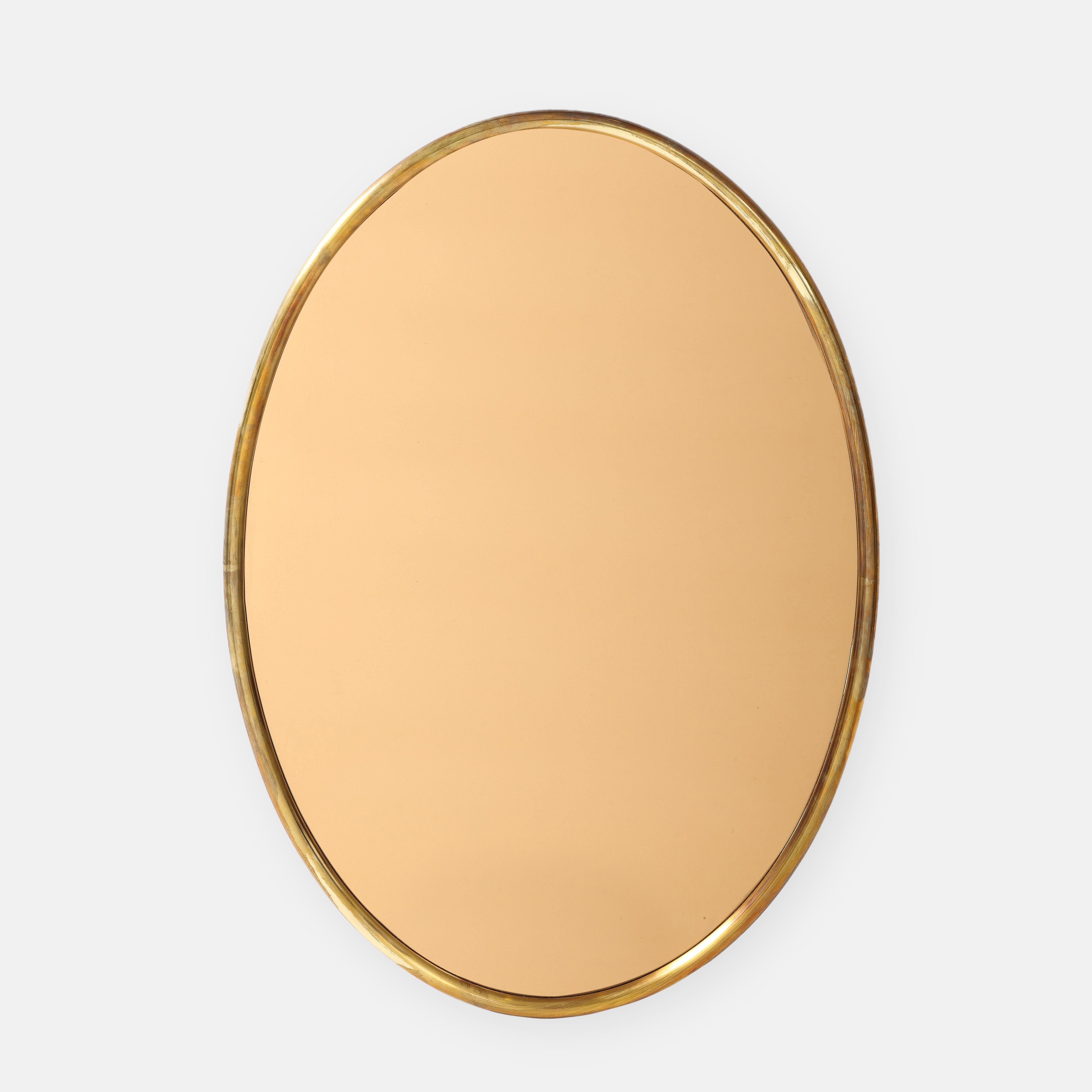 1970s Italian large oval mirror with thick rounded lacquered brass frame and rose gold mirrored glass with wood backing.  This chic mirror has a lovely patina to the lacquered brass which contrasts beautifully with the elegant rose gold color or the