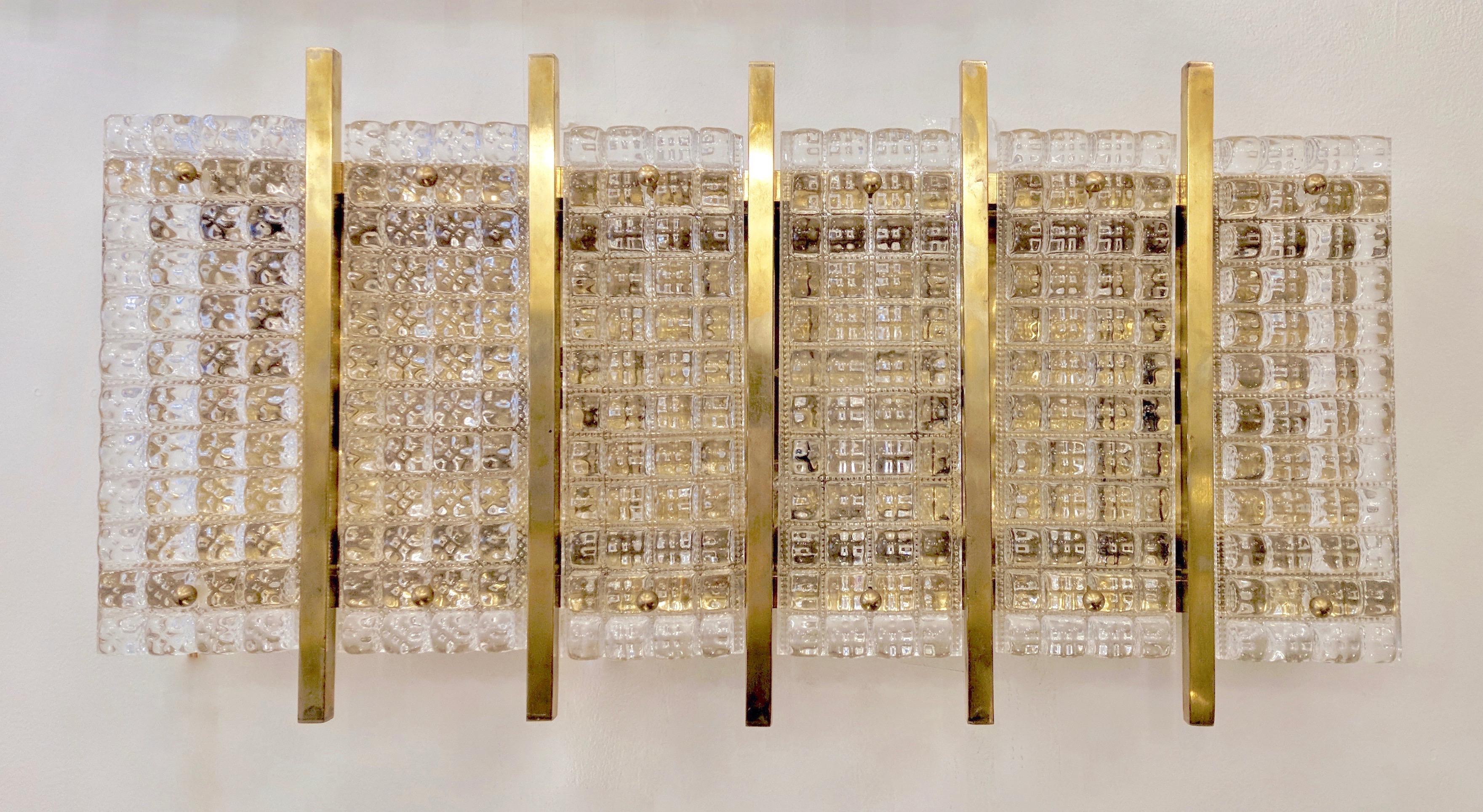 Italian mid-Century modern design wall lights, entirely handmade; 3D textured clear Murano glass molded panels are mounted on a brass support interspersed with solid brass bars to create a unique sleek design. High quality of craftsmanship.
3