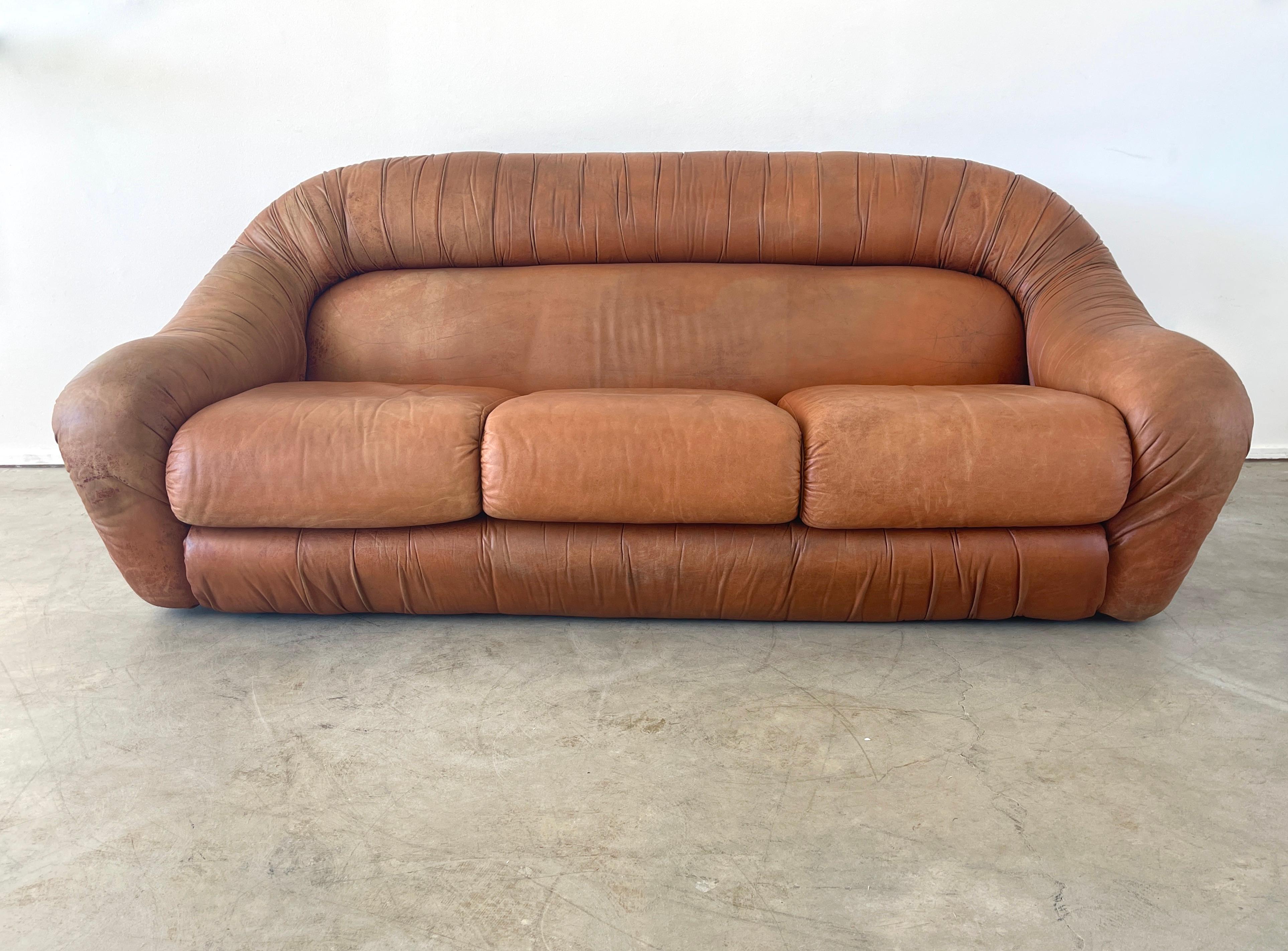 Italian 1970's three-seater sofa in caramel brown leather with a seat cushion and side armrests integrated with the sculptural curved backrest. 
Great shape - original vintage condition with wonderful patina.
 