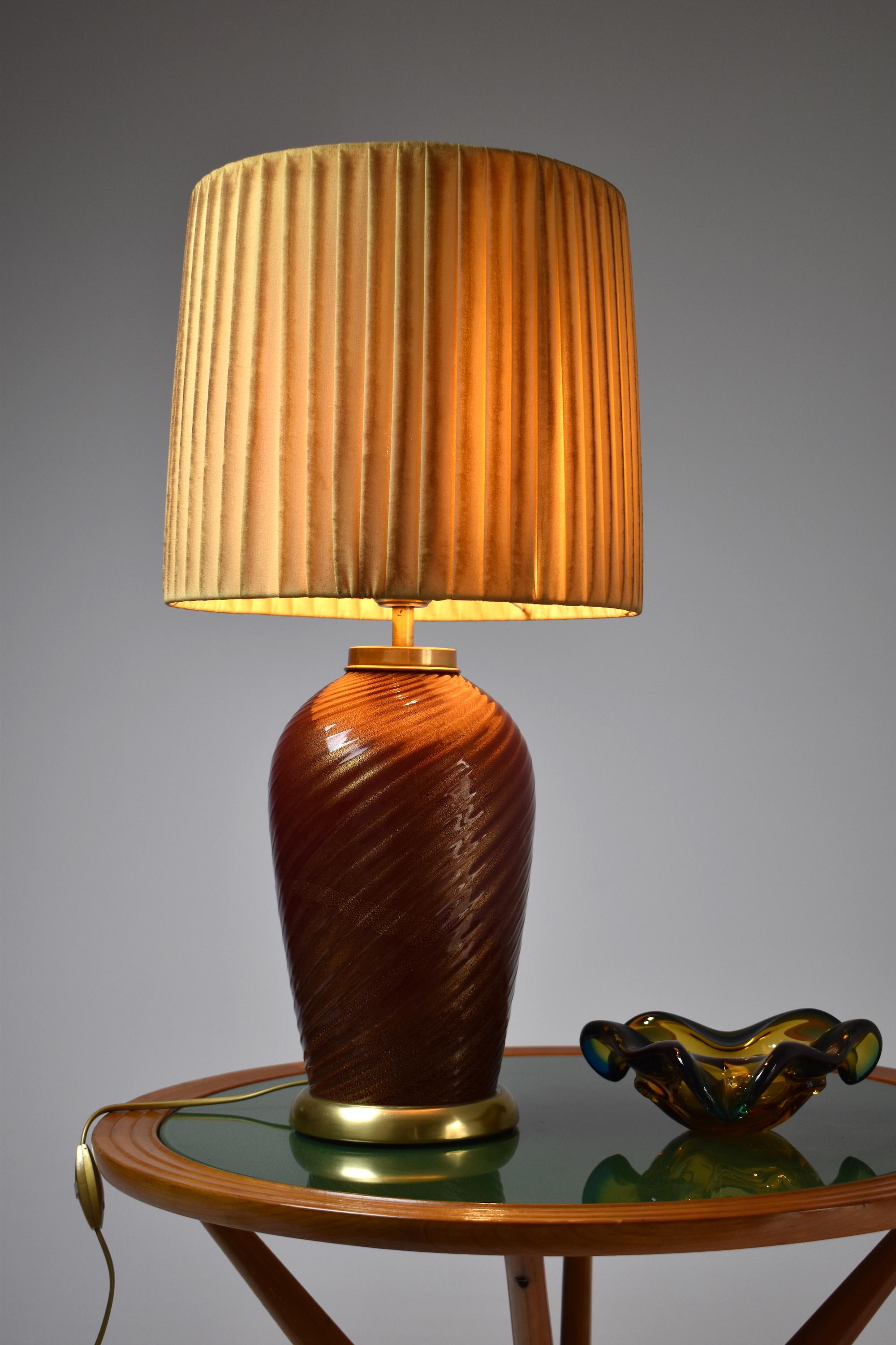 A magnificent 20th-century vintage table lamp by notable Italian designer Tommaso Barbi circa 1970's. This stand-out lighting piece is crafted with a Murano burnt orange dark red swirl glass with gold shimmers all over and polished brass rims.