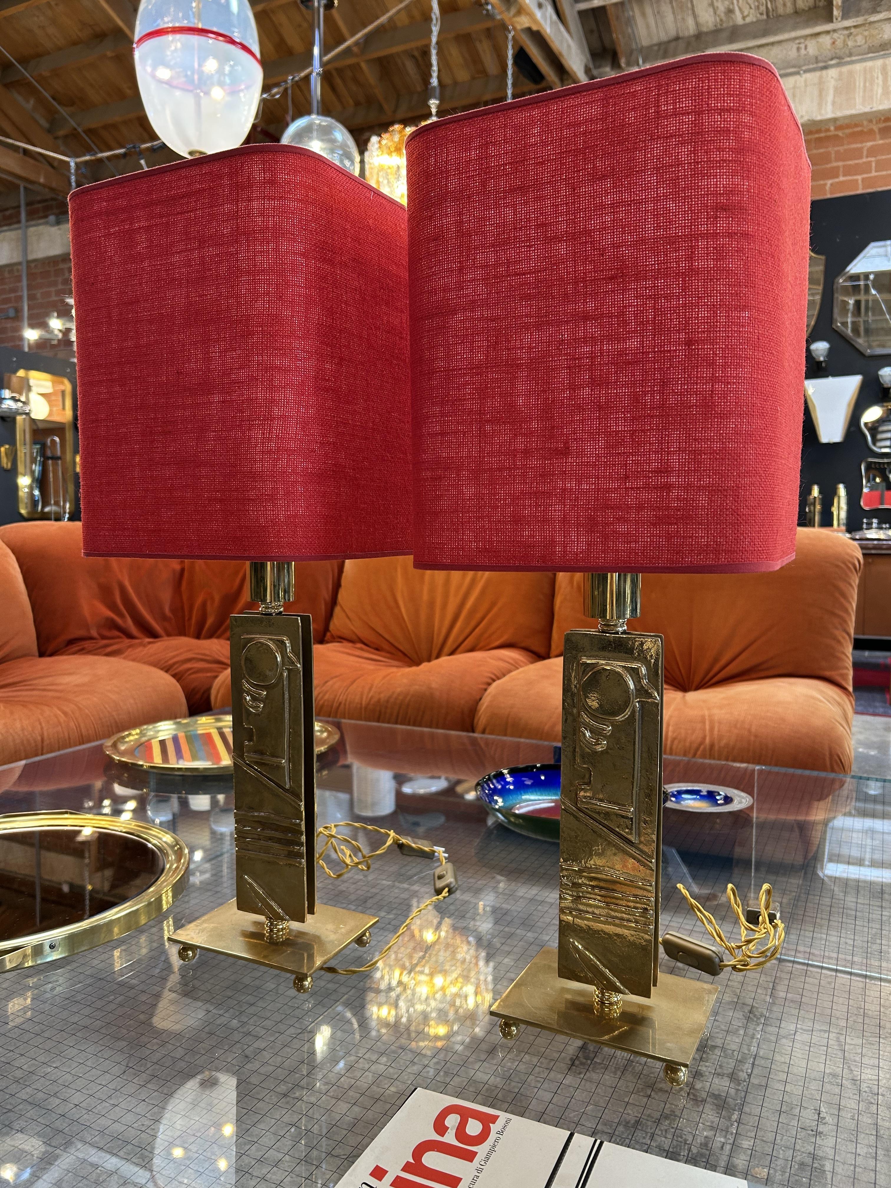 Questa splendida coppia di lampade da tavolo italiane del Mid-Century Modern degli anni '70 presenta basi scultoree in ottone ornate da dettagli astratti che ricordano i motivi di antichi templi. Le audaci tonalità rosse del lino creano un contrasto
