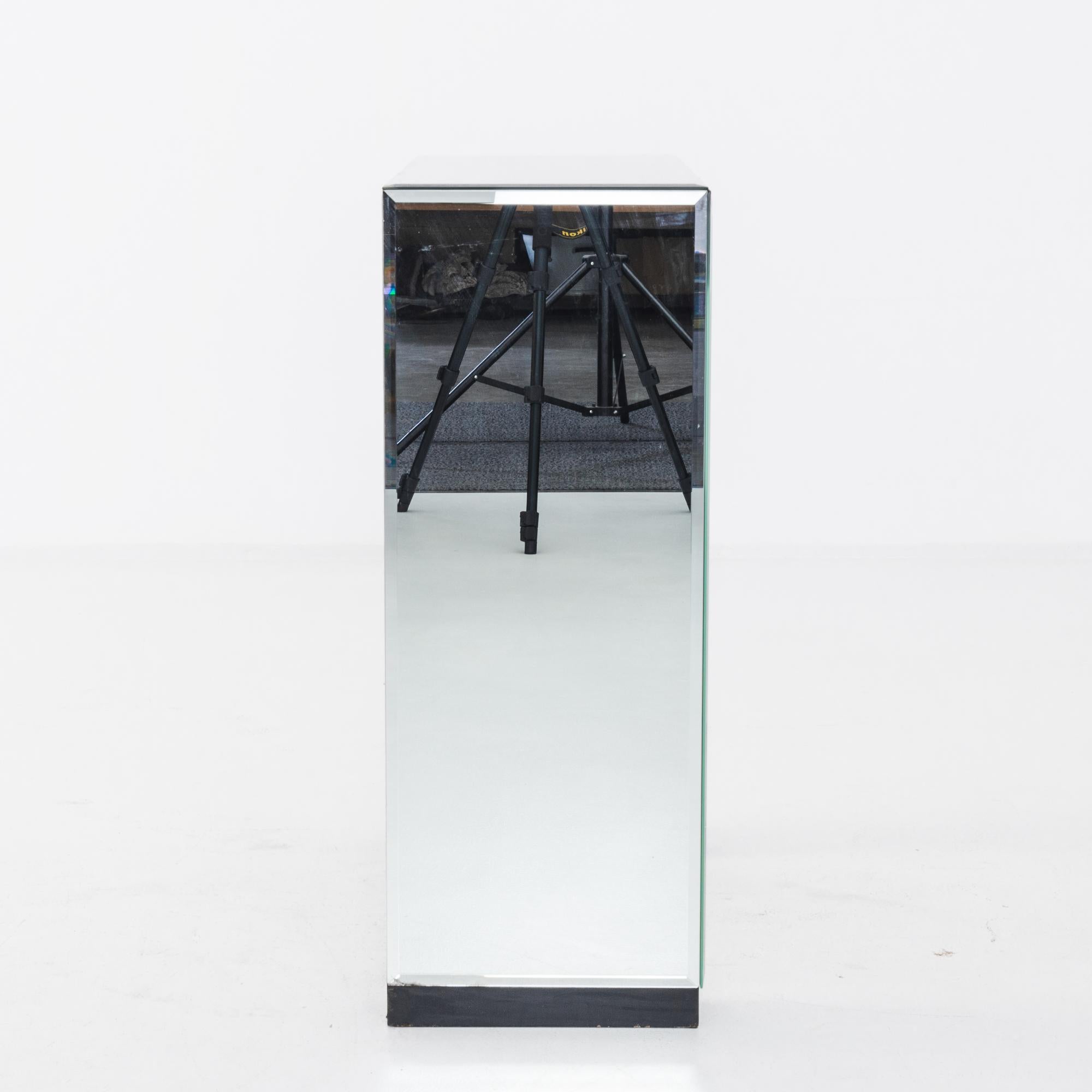 A mirrored glass console table produced in Italy circa 1970. Like a massive cut gem winking in the sunlight, this distinctive console table catches the eye immediately. From its unique silhouette–two supports standing like twin trunks around a tall,