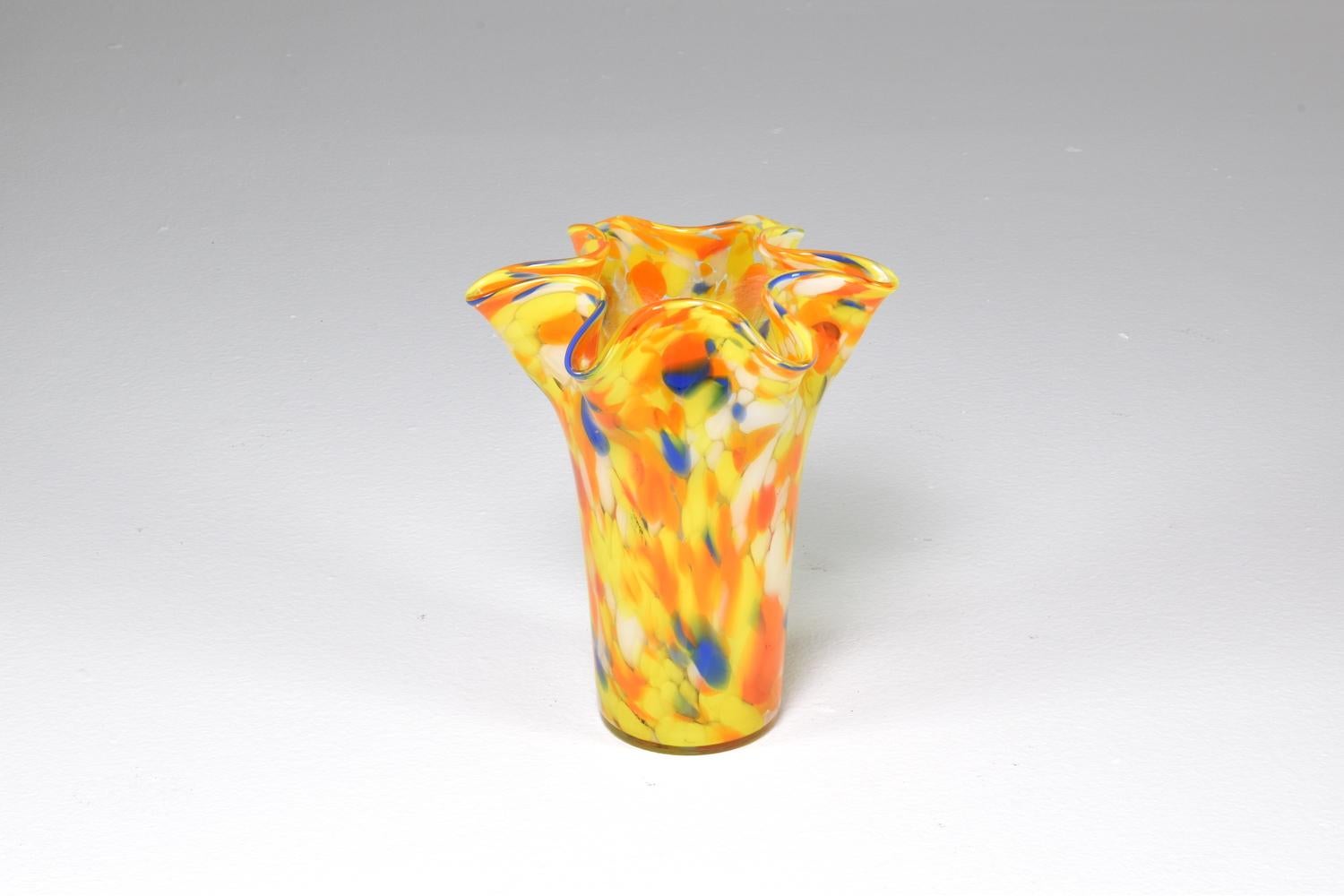Vase aus mundgeblasenem italienischem Glas aus den 1970er Jahren mit farbenfrohen Flecken aus Murano-Glas in Orange-, Gelb-, Weiß- und Blautönen, die gekonnt miteinander vermischt wurden. 
Dieses fröhliche Dekorationsstück ist in Form einer