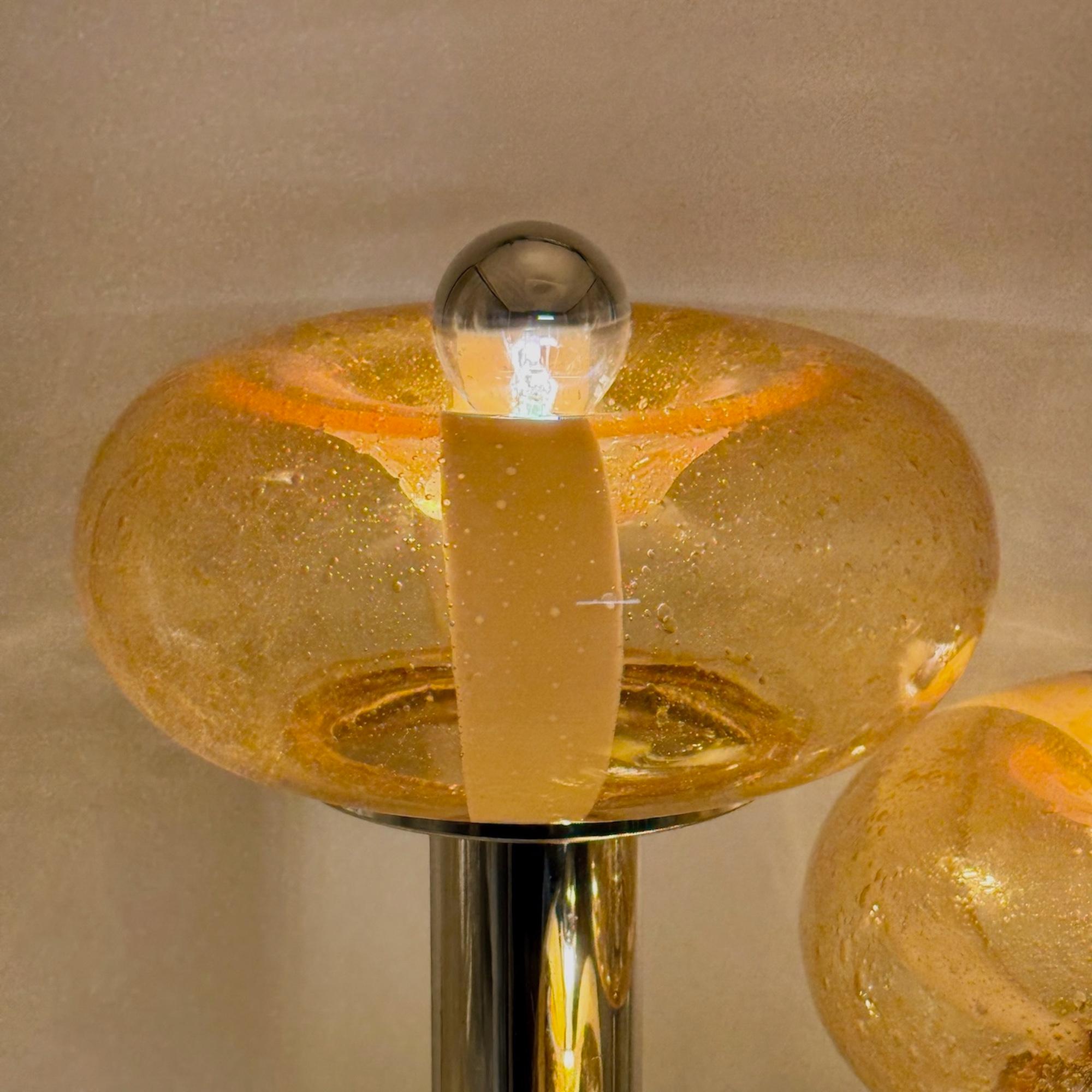 Questa rara lampada in vetro di Murano e cromo degli anni '70 è un esempio scultoreo di design italiano dell'illuminazione, che fonde funzionalità e audace espressione artistica. La struttura cromata sostiene tre bracci verticali, ognuno dei quali è