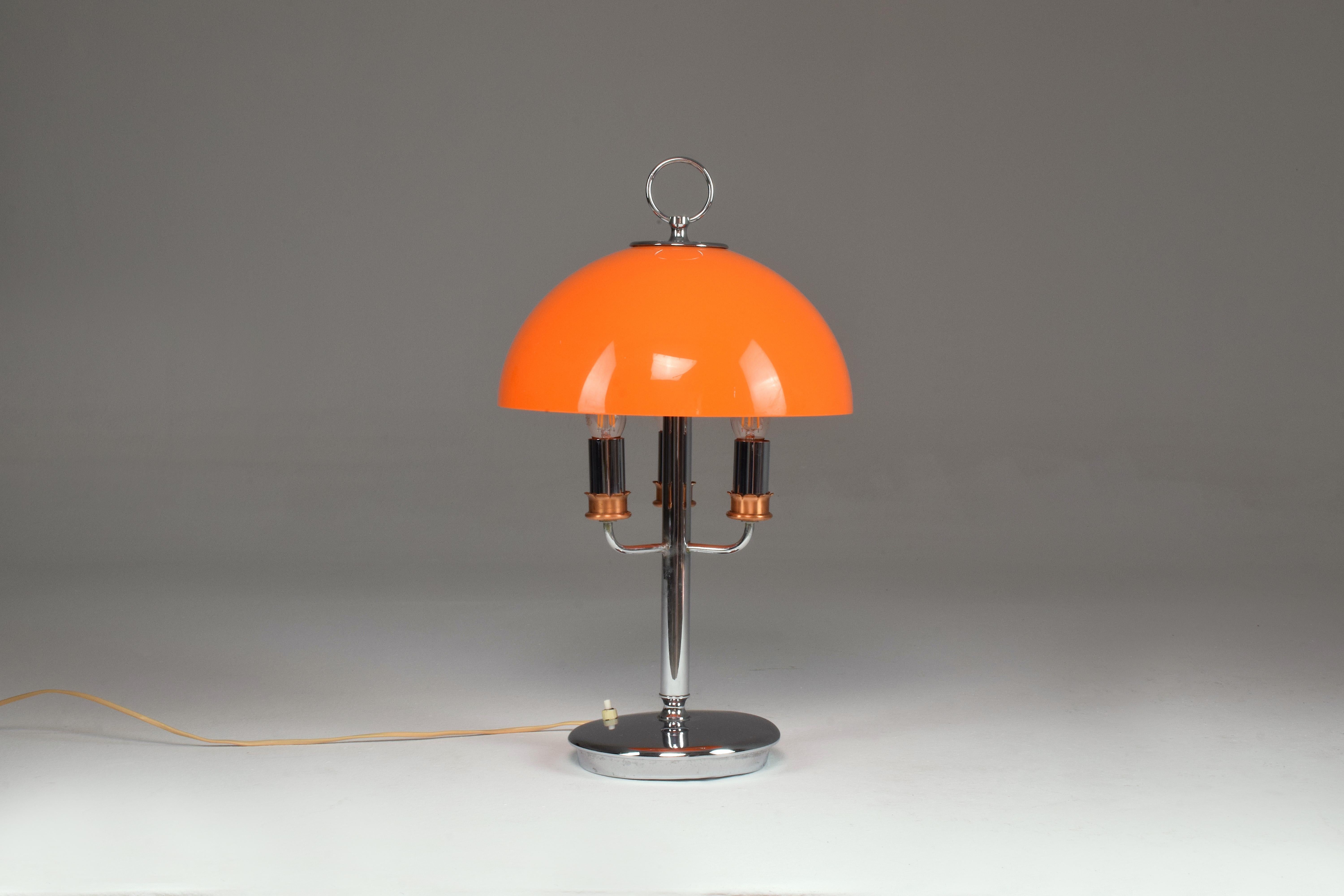 A super stylish space age style 20th-century vintage Italian table lamp designed with an orange plexiglass shade, a metal carrier handle at the top, and three-light source inputs. 
The structure is in chrome brass and is teamed with a push-type