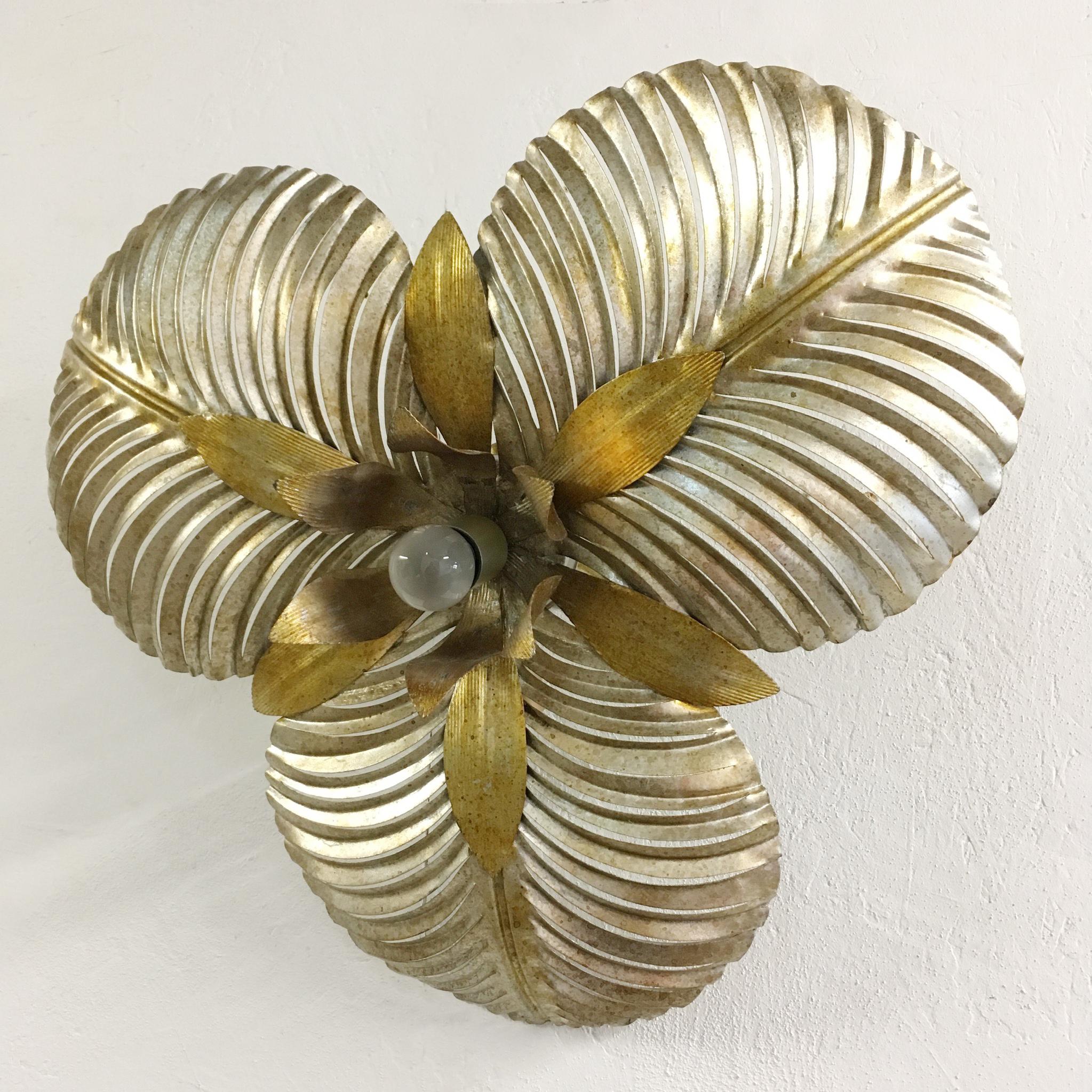 Tropical gilt palm leaf ceiling light, circa 1970s, Italian.
Stunning large palm shaped leaves with cut out detail for light to pour through.
The leaves surround a bud of golden petals that carry a single bulb holder.
On the back of the light