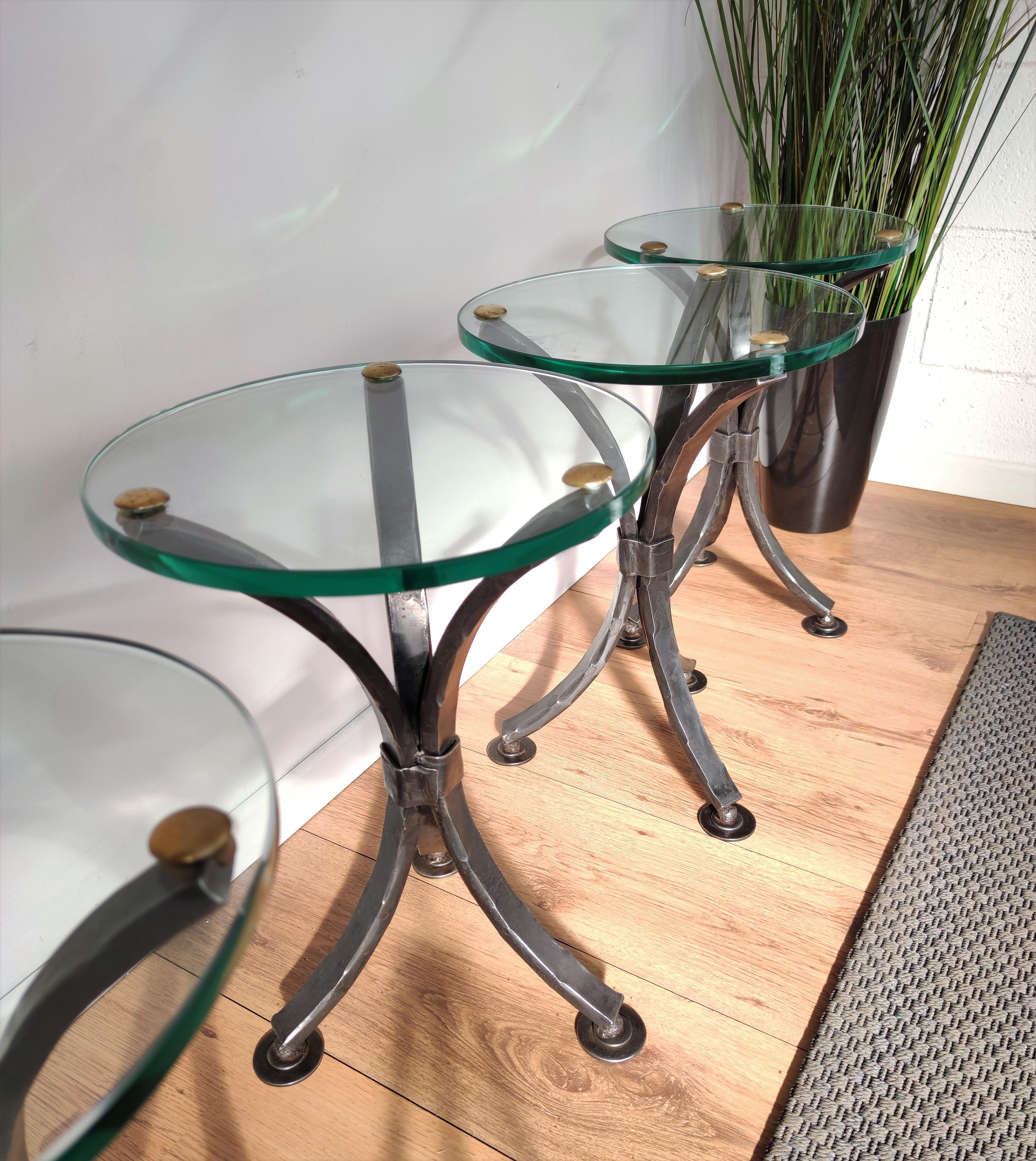 Beautifully hand crafted wrought iron round tripod pedestal side tables with strong and thick glass top, fixed with decorative brass nails. The 3 legs, greatly shaped and forged with the typical finish of hand forging, are finished with round feet