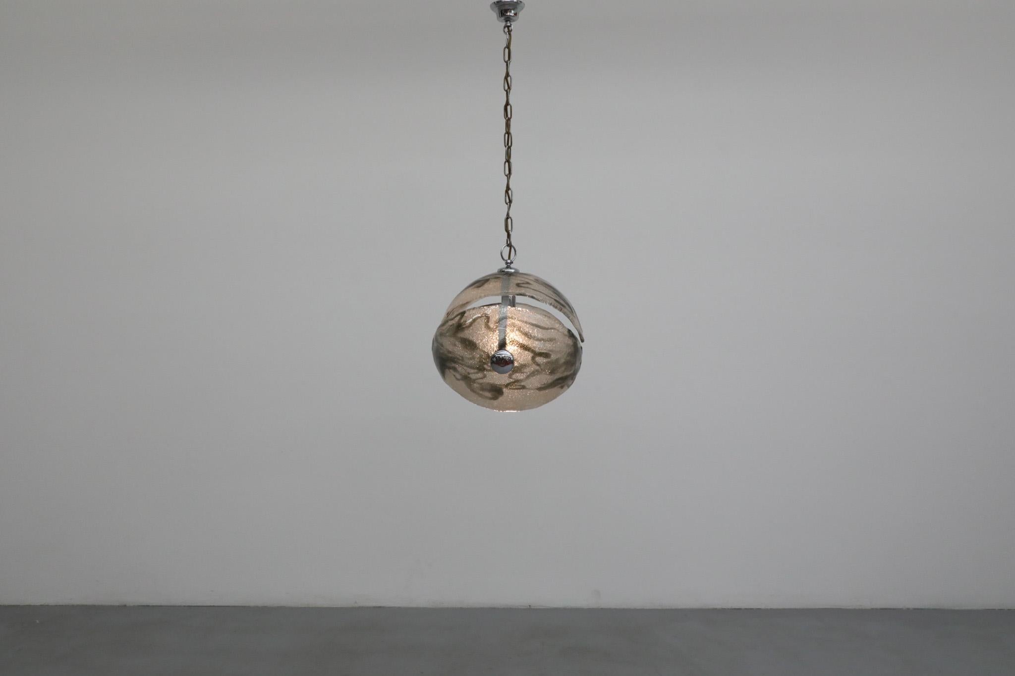 Pendente a sfera moderno e spaziale italiano degli anni '70. Tre grandi fette di vetro fuso selvaggiamente marmorizzato grigio e semitrasparente circondano una cornice cromata e formano un grande casco. Completa di una lunga catena cromata e di un