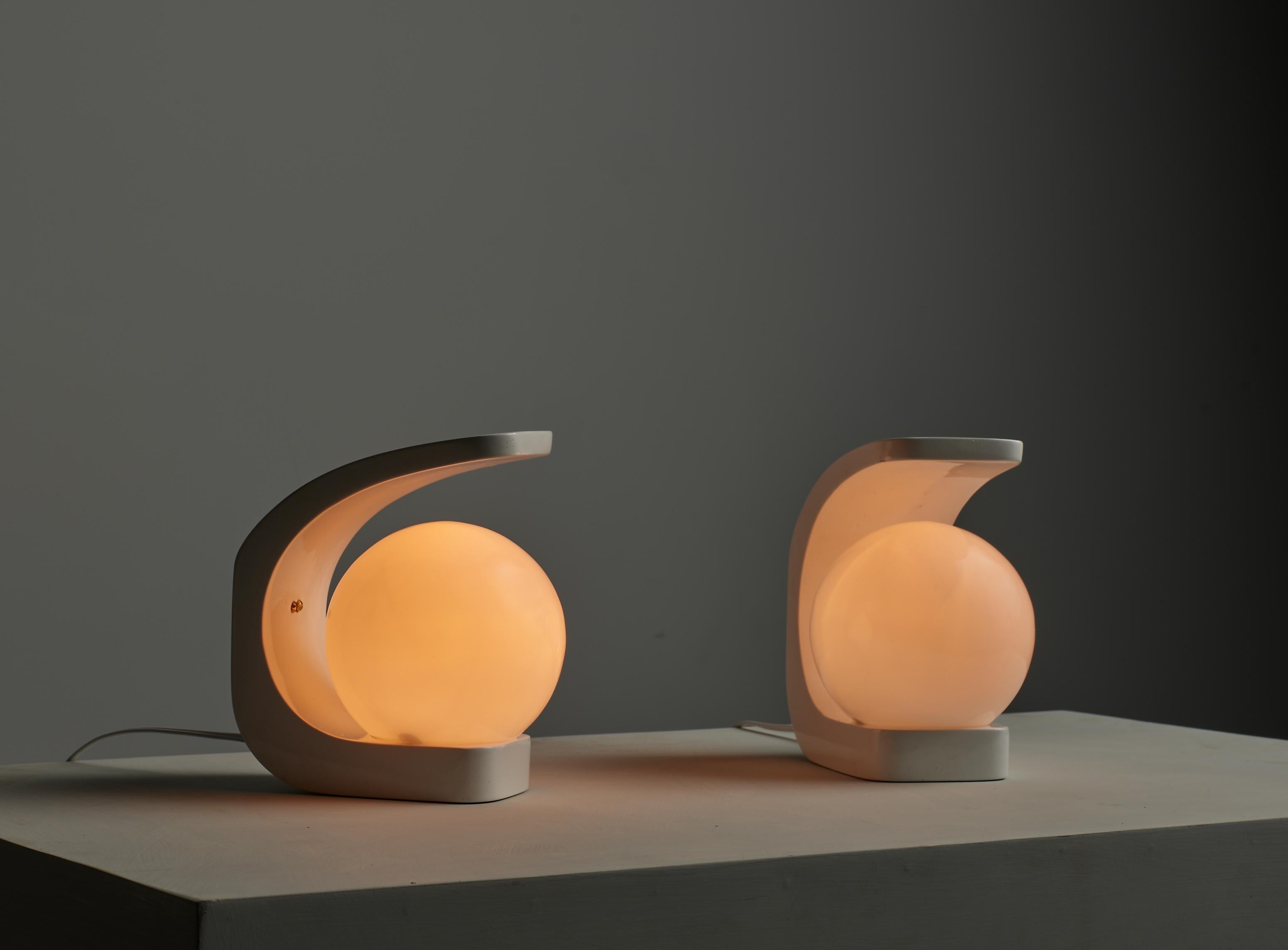 This listing features a pair of Italian table lamps from the 1970s, showcasing a minimalist yet sophisticated design. The lamps are crafted from white lacquered wood, with a curved structure that elegantly encloses a spherical opaline glass shade,