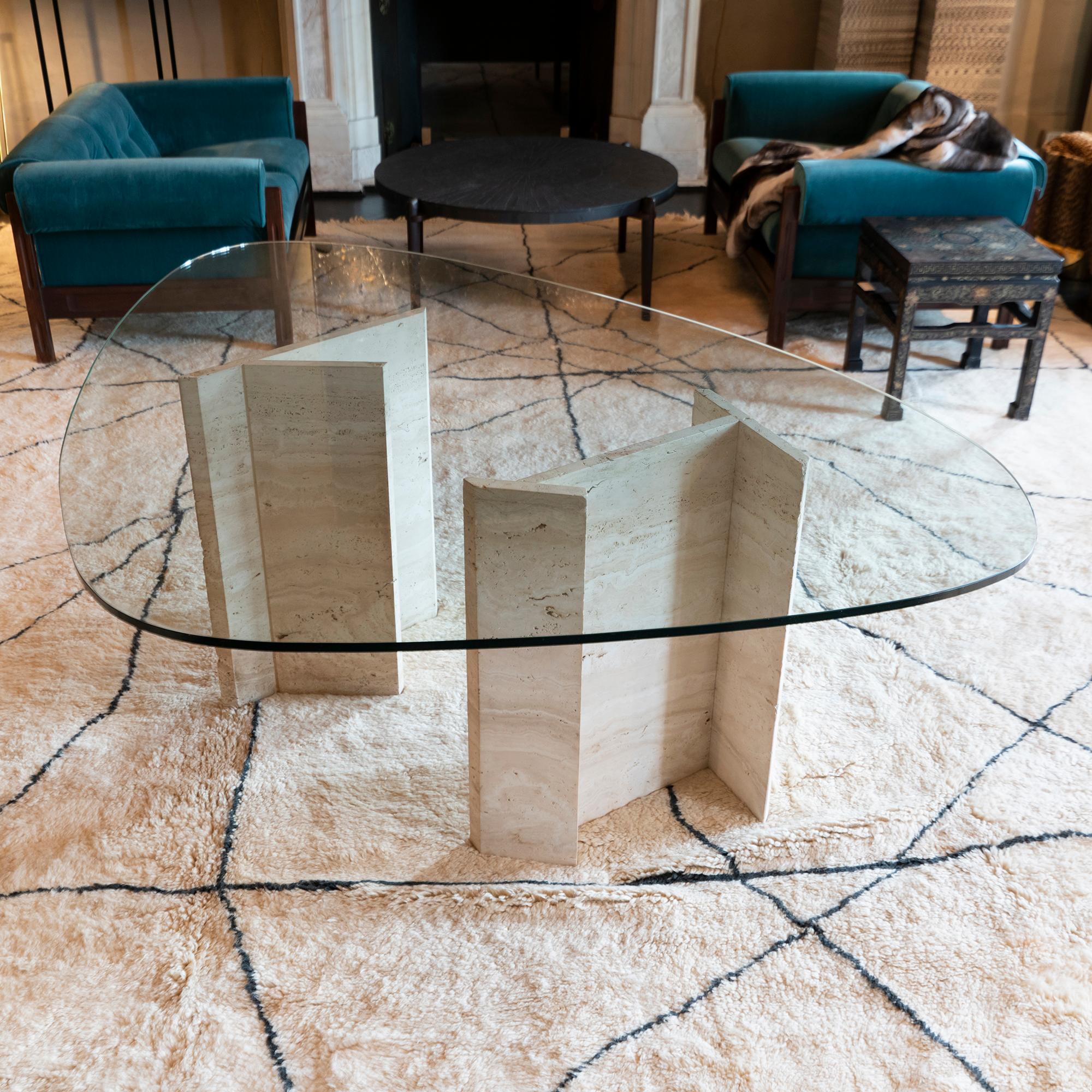 Sculptural center table with geometrical travertine bases in perfect condition and vintage patina, some chipping on both bases as showed, heavily scratched surface oval shape glass top, Italy, circa 1970.