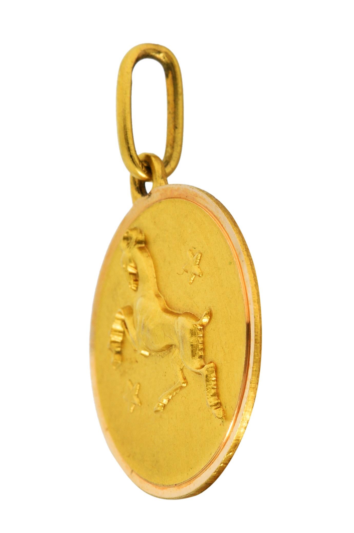 Circular charm has a matte finish and a raised rendering of a ram

Reared on its hind legs and accented by two stars

With a brightly polished border

Italian assay marks for 18 karat gold

Circa: 1970s

Measures: 5/8 x 7/8 inch (including jump ring
