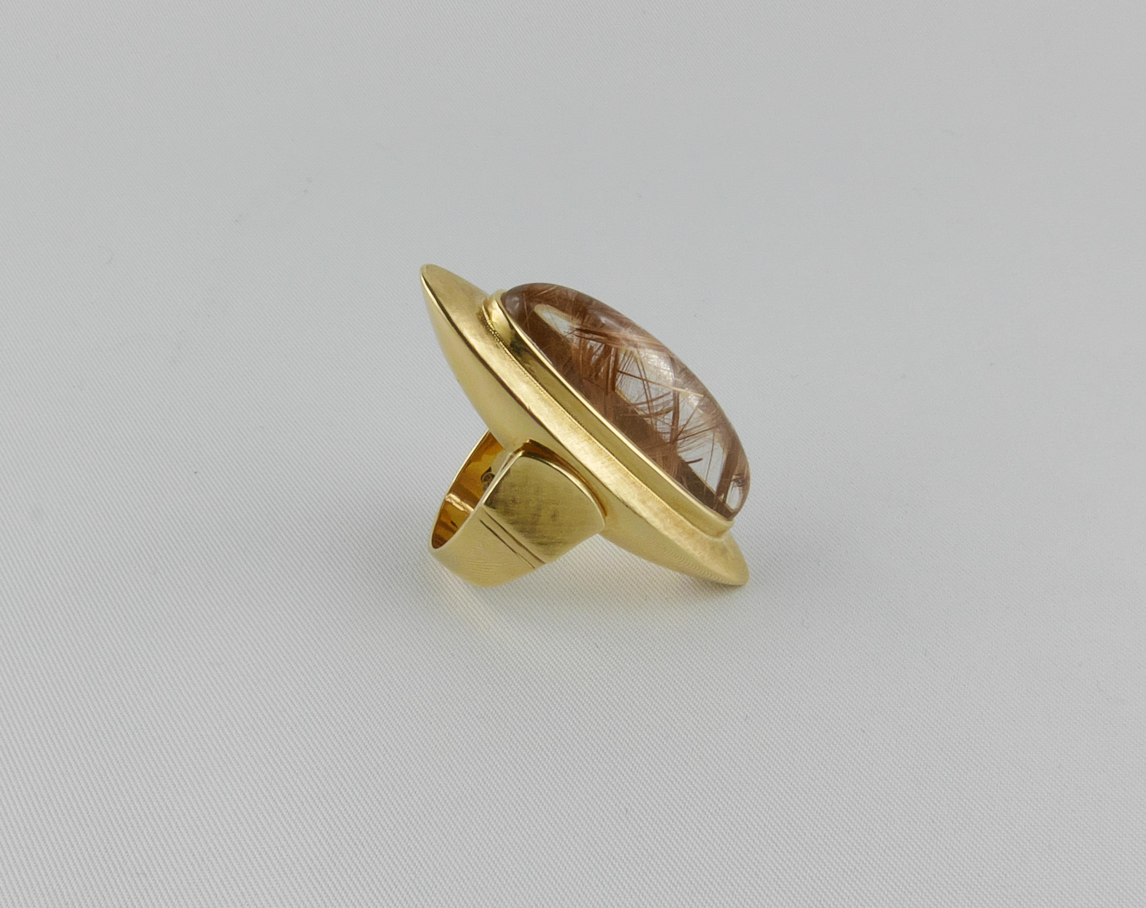 This eye-catching oval shaped Ring is a fine example of 1970s geometric audacious and beautiful design. Finely crafted in Italy  in 18k chunky satin textured Yellow Gold. The Ring is centered with an imposing Rutilated Quarz oval cabochon. This