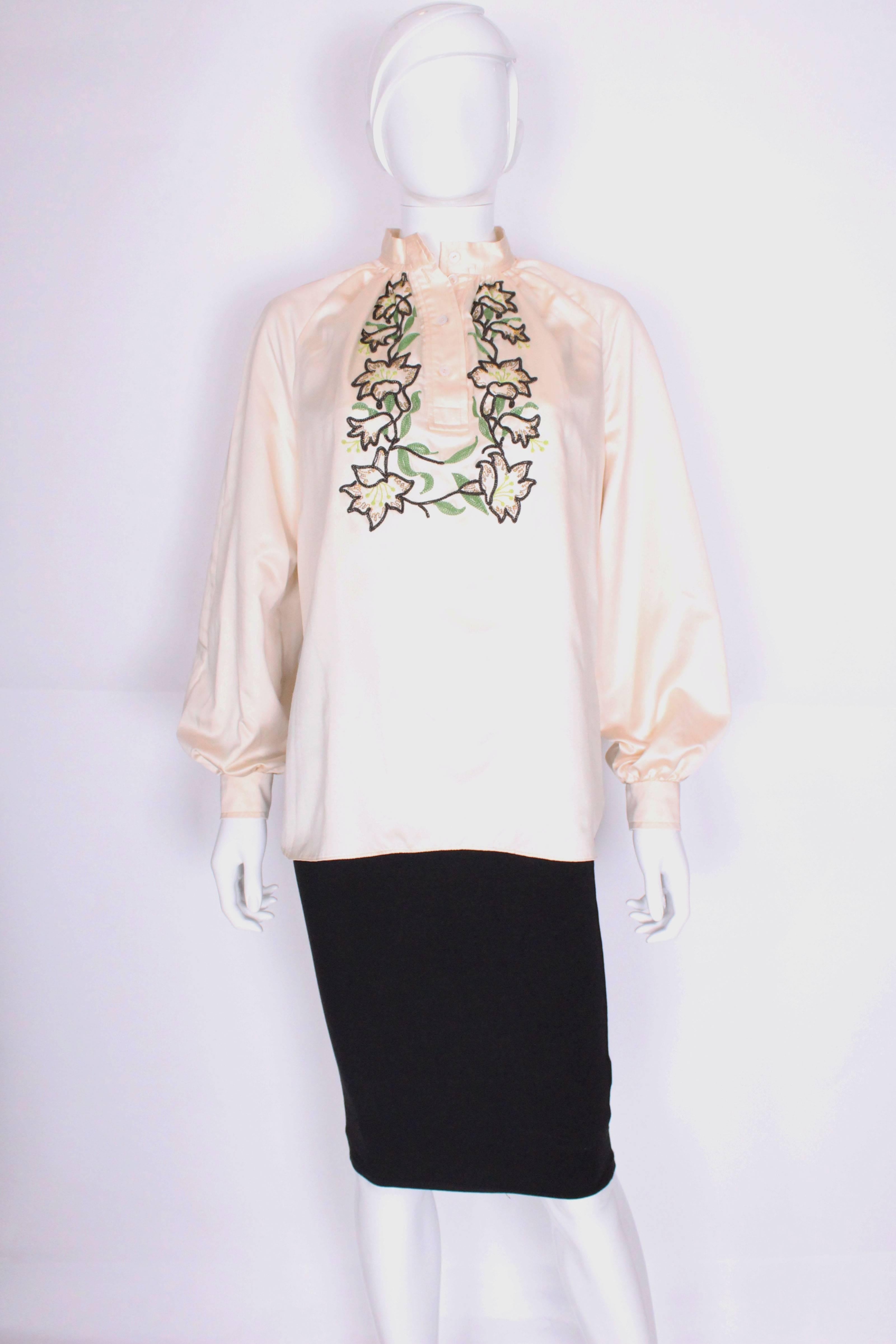 An elegant and easy to wear blouse by British designer Caroline Charles. In a lovely ivory colour, this blouse has a mandarin collar, with a 4 button opening. There is floral embroidery detail on the front in browns and greens. The cuffs are have a