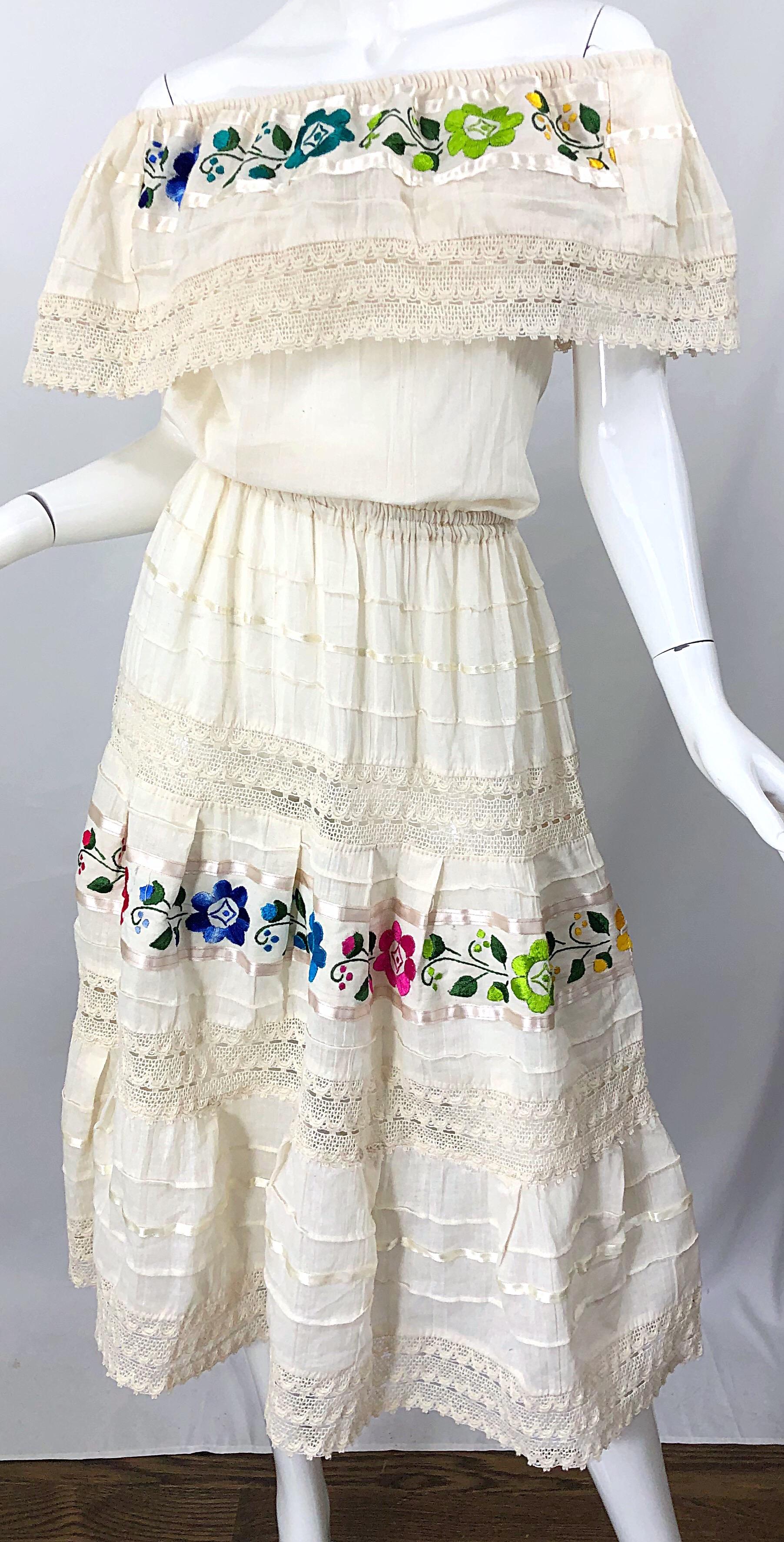 Schickes, elfenbeinfarbenes, mit Blumen besticktes schulterfreies Kleid im spanischen Boho-Stil aus den 70er Jahren! Schmeichelhaftes, locker sitzendes Mieder mit Gummizug an Schultern und Taille. Leuchtend bunte Blumen in Lila, Blau, Grün, Rosa,