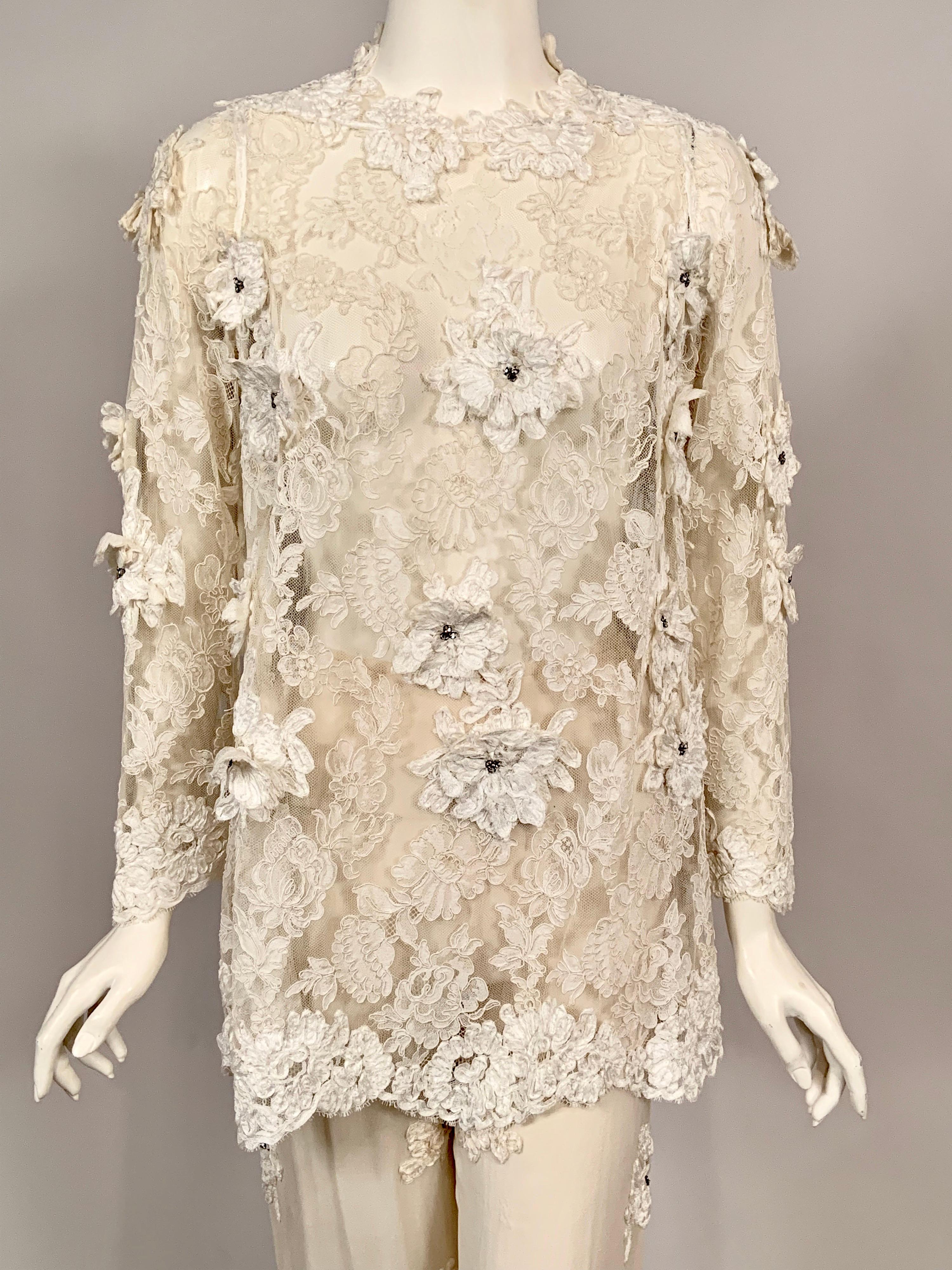 A sheer ivory lace top is appliqued with white silk ribbon flowers and prong set rhinestone centers. It is collarless with long sleeves and closes at the center back with snaps following the design of the lace. The flowing ivory chiffon pants have a