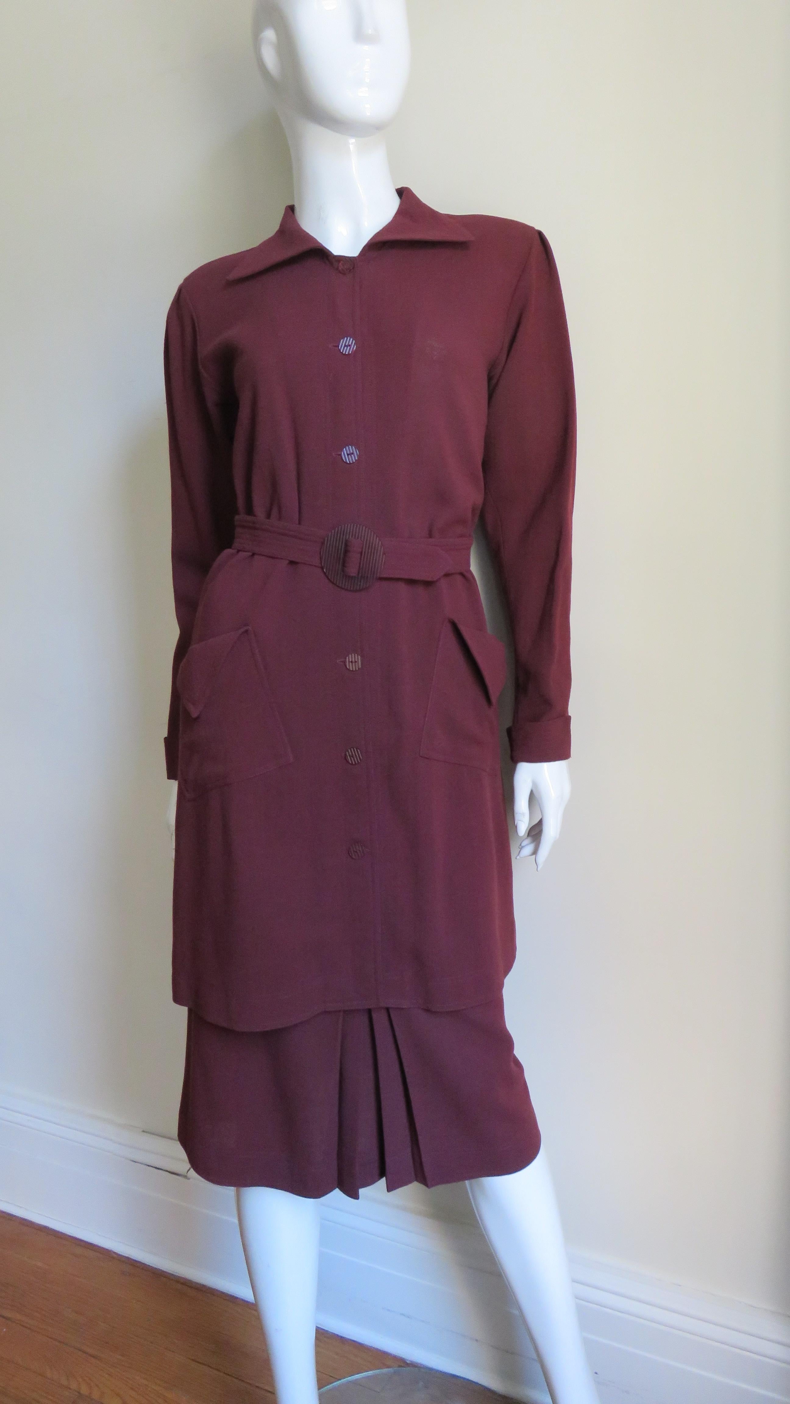 A great burgundy colored wool skirt suit by Jean Muir.  The jacket has long sleeves with folded back cuffs, tucks at the tops of the shoulders with slight padding and a shirt collar.  It is lower thigh length with 2 front flap pockets, matching
