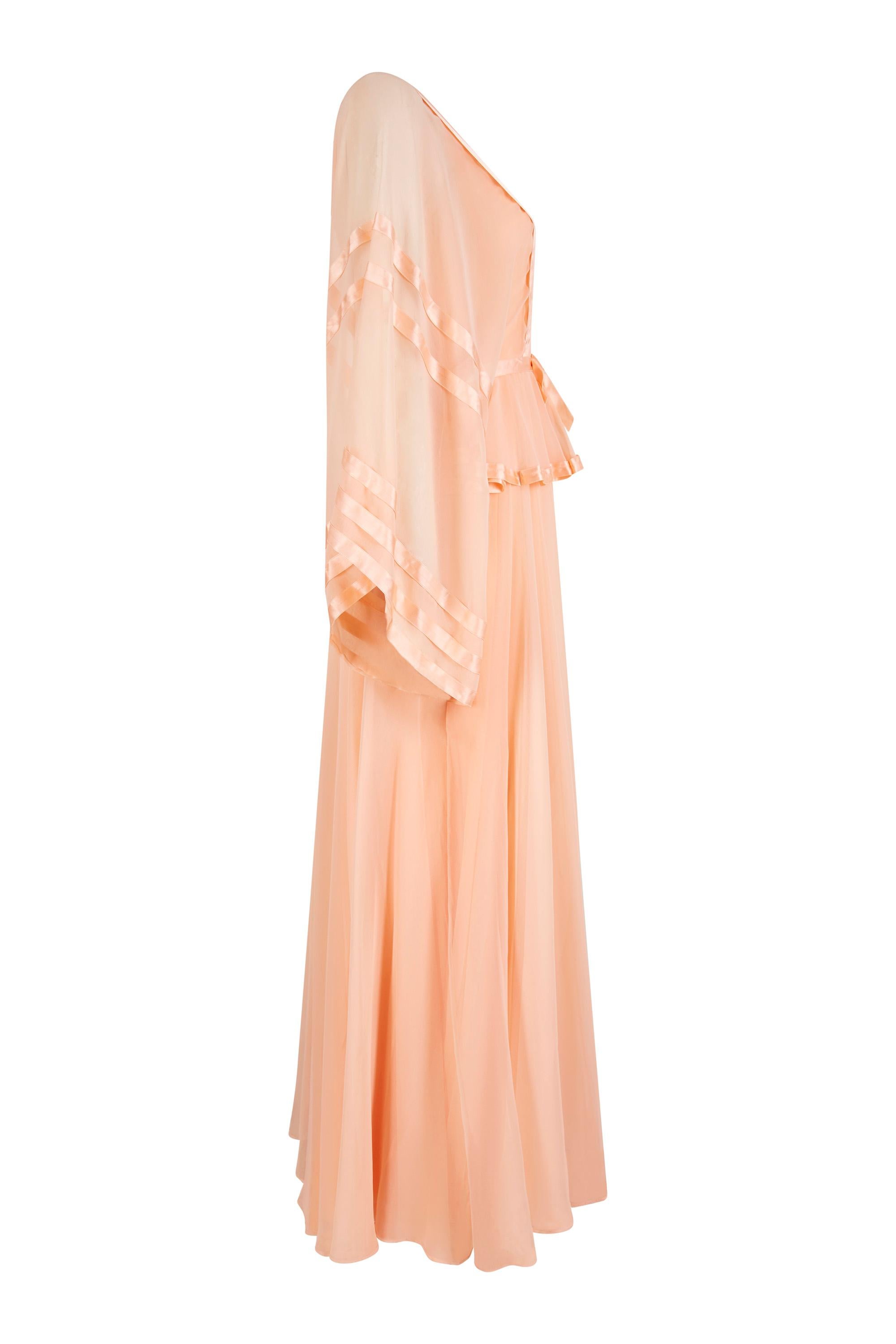 Cette captivante robe en mousseline de soie pêche pâle des années 1970, bordée de rubans, est signée du label britannique Jean Varon et constitue un bel exemple du penchant du créateur pour les lignes féminines plus douces, synonymes de son travail