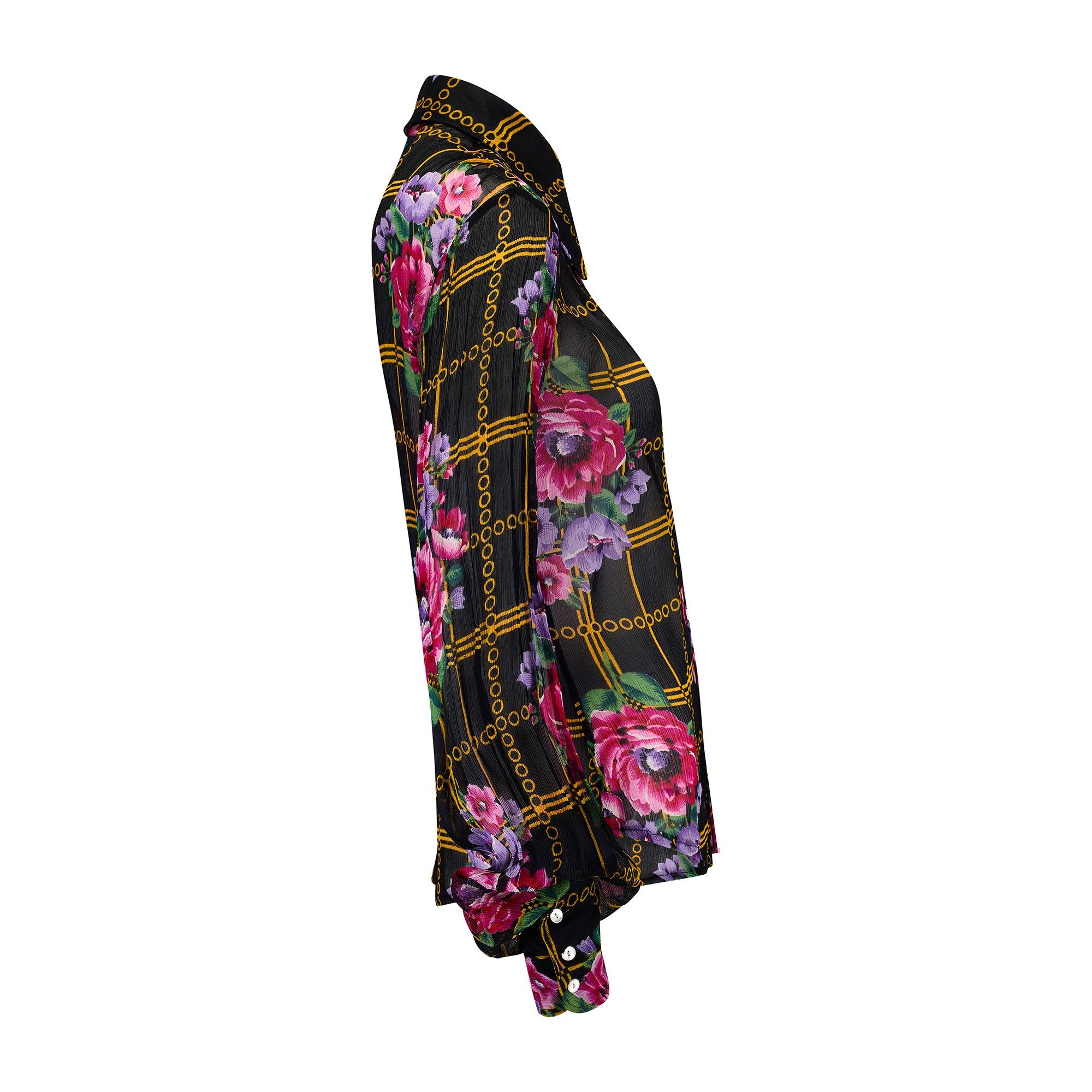 This bold, floral patterned blouse was designed by celebrated British designer Jeff Banks during the 1970s. It is tailored from sheer black chiffon printed with fuchsia and violet flowers and yellow geometric shapes. The chiffon is subtly plissé