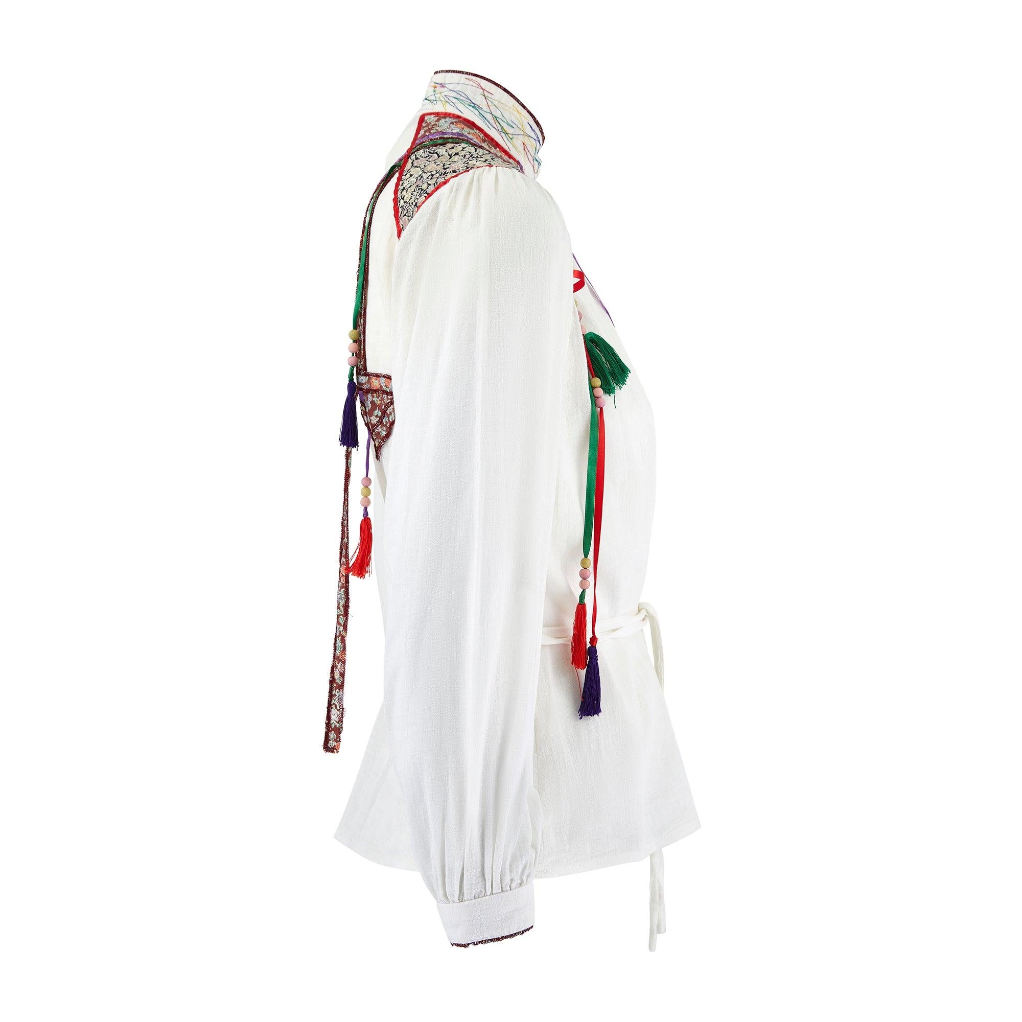This quirky 1970s shirt is by celebrated British designer Jeff Banks. Tailored from white muslin or cheesecloth cotton, it is trimmed with a geometric patchwork design in floral Liberty print cloth across the shoulders, inside the cuffs, the collar
