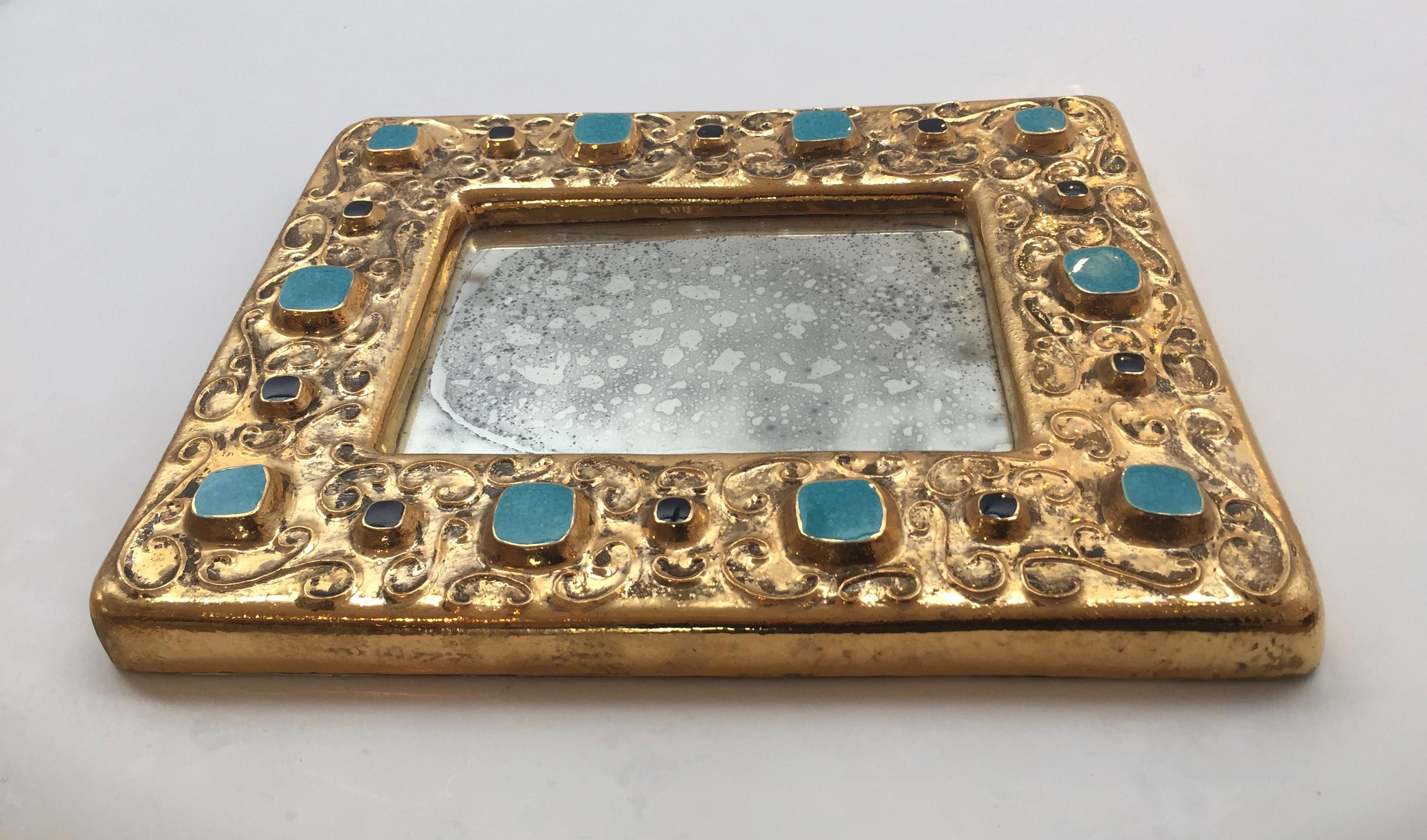 Gilt glazed ceramic mirror surround, 'studded' with turquoise and jet 'jewels' in high relief amongst scrolling tendrils.
Incised signature in facsimile on the back 'F Lembo'.