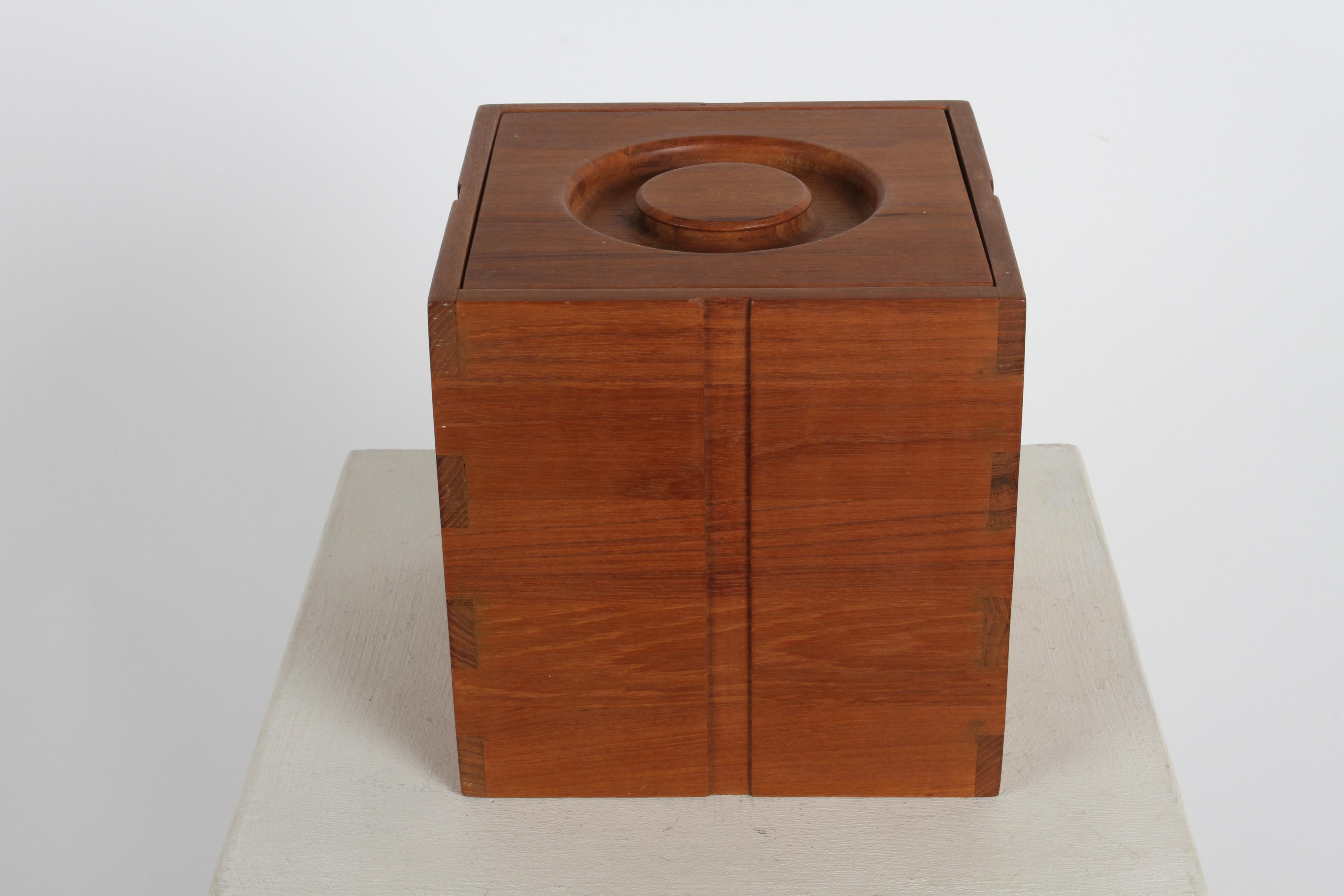 1970s Kalmar Designs Danish Modern style teak wood ice bucket with original thongs and removable plastic liner. Having concentric circle removable lid, brown plastic liner, and wonderful finger joint corners. Appears to have little to no use, label