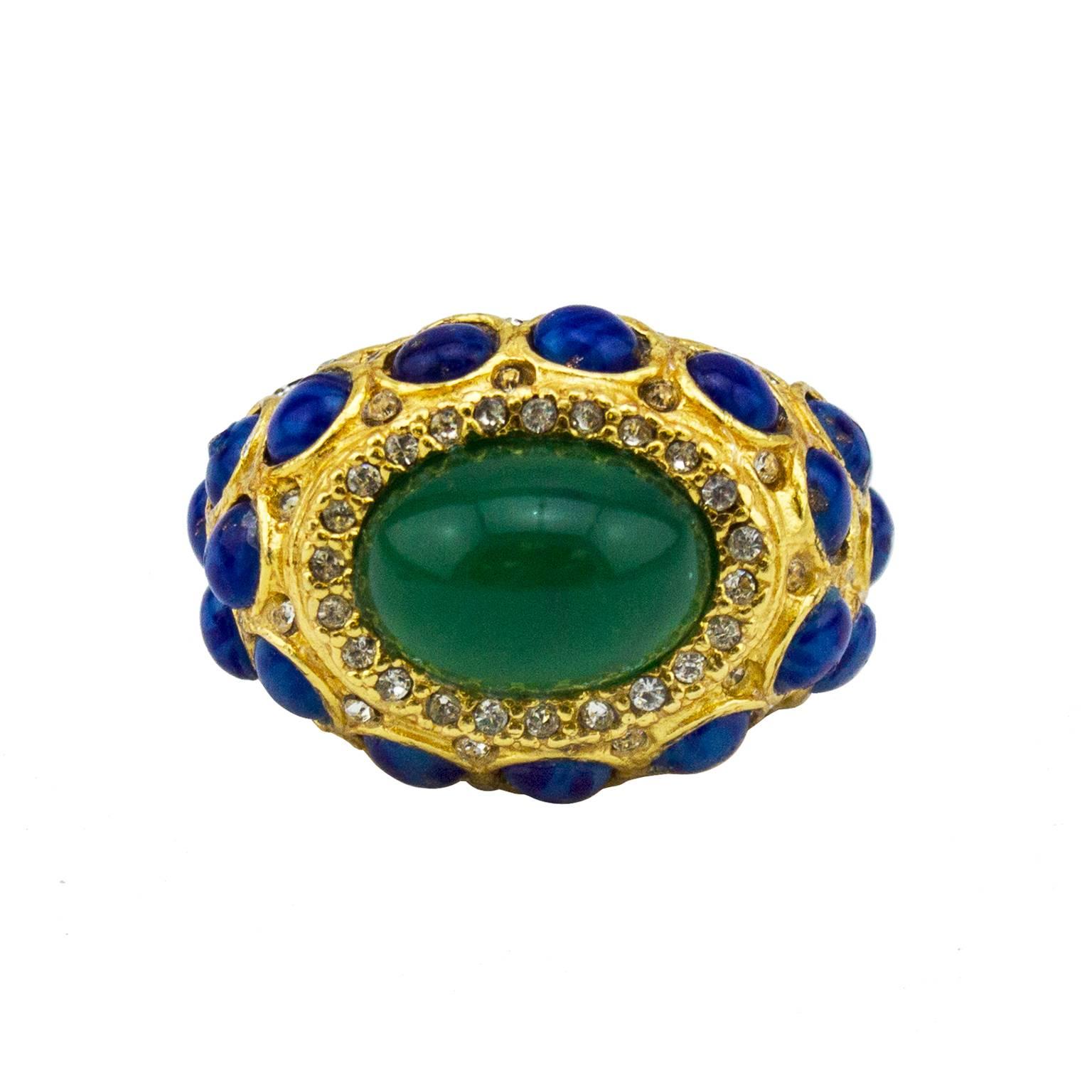 Stunning 1970s Kenneth Jay Lane cocktail ring. Gold tone metal embellished with tiny rhinestones and cobalt blue stones. One large emerald green stone featured in centre with more tiny rhinestones around the perimeter. K.J.L plaque on interior.