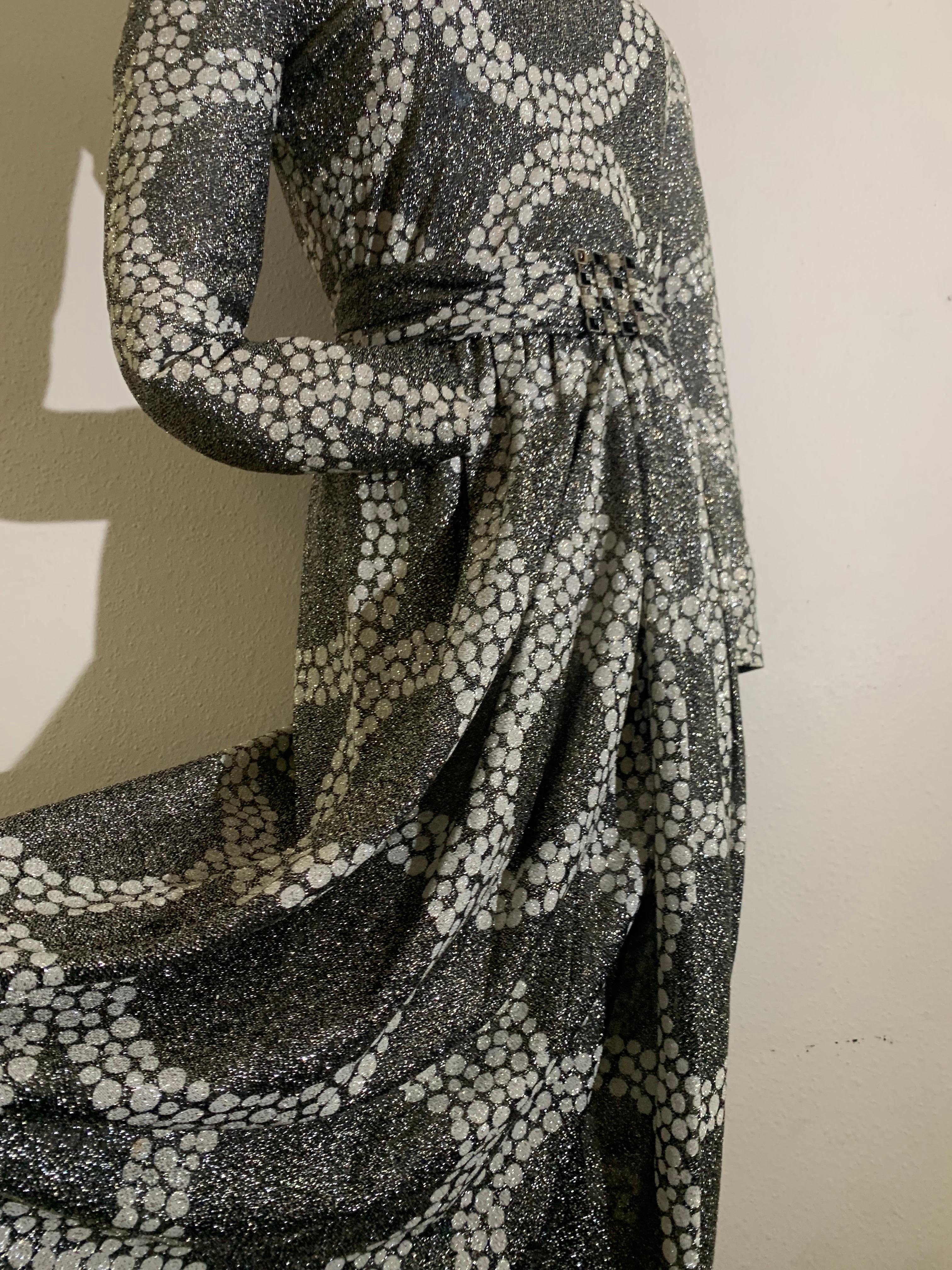 Maxivestido de punto de lúrex plateado Kiki Hart de los años 70 con grandes motivos circulares de guijarros:  Un fabuloso modelo de punto novedoso en Lúrex brillante con cuello alto, mangas largas, falda delantera fruncida en cascada y cinturón