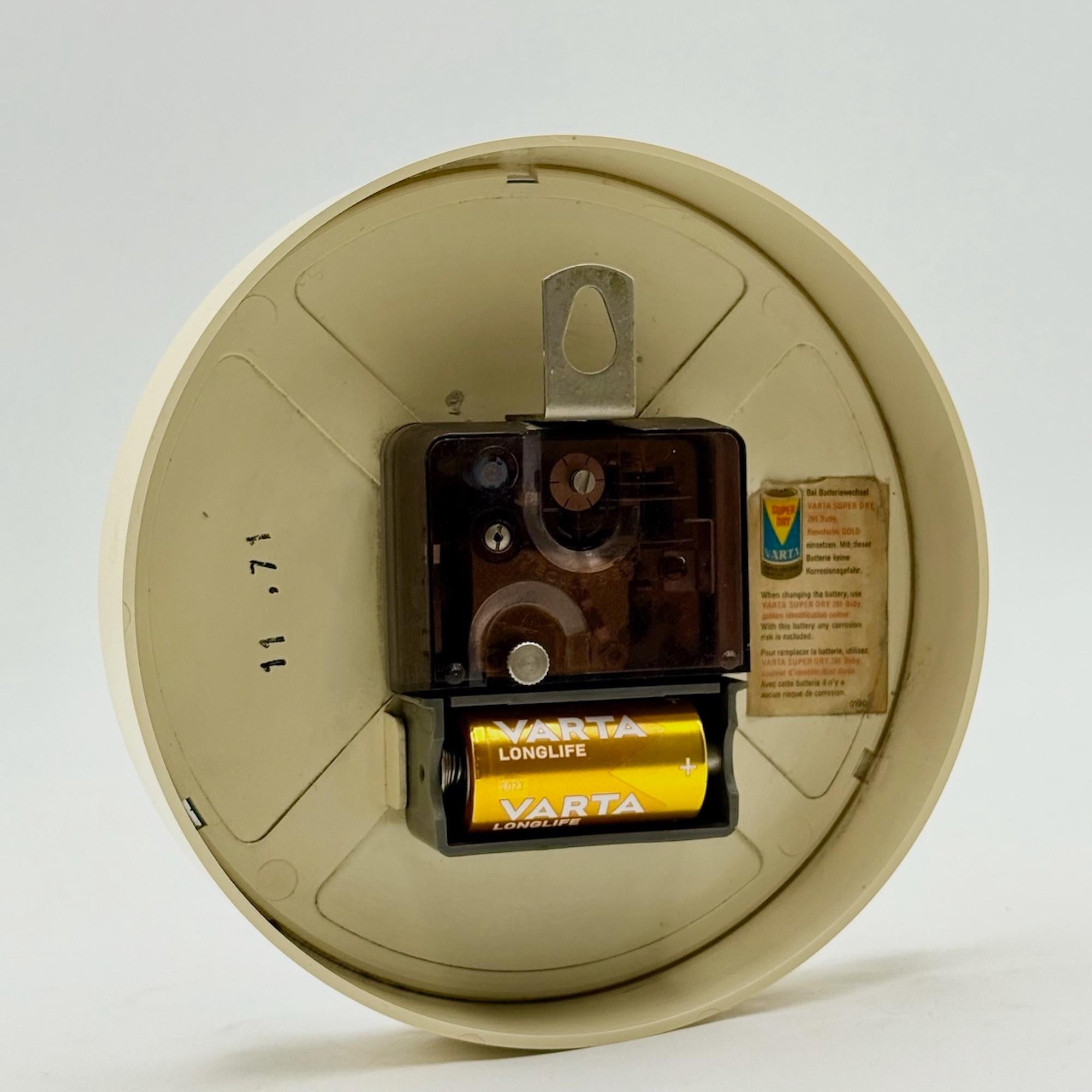 Experience the iconic design of the Seventies with this space age wall clock by Krups, made in West Germany in November 1973. 

Featuring a round green dial framed in beige with distinctive graphics, this vintage wall clock is a striking example of
