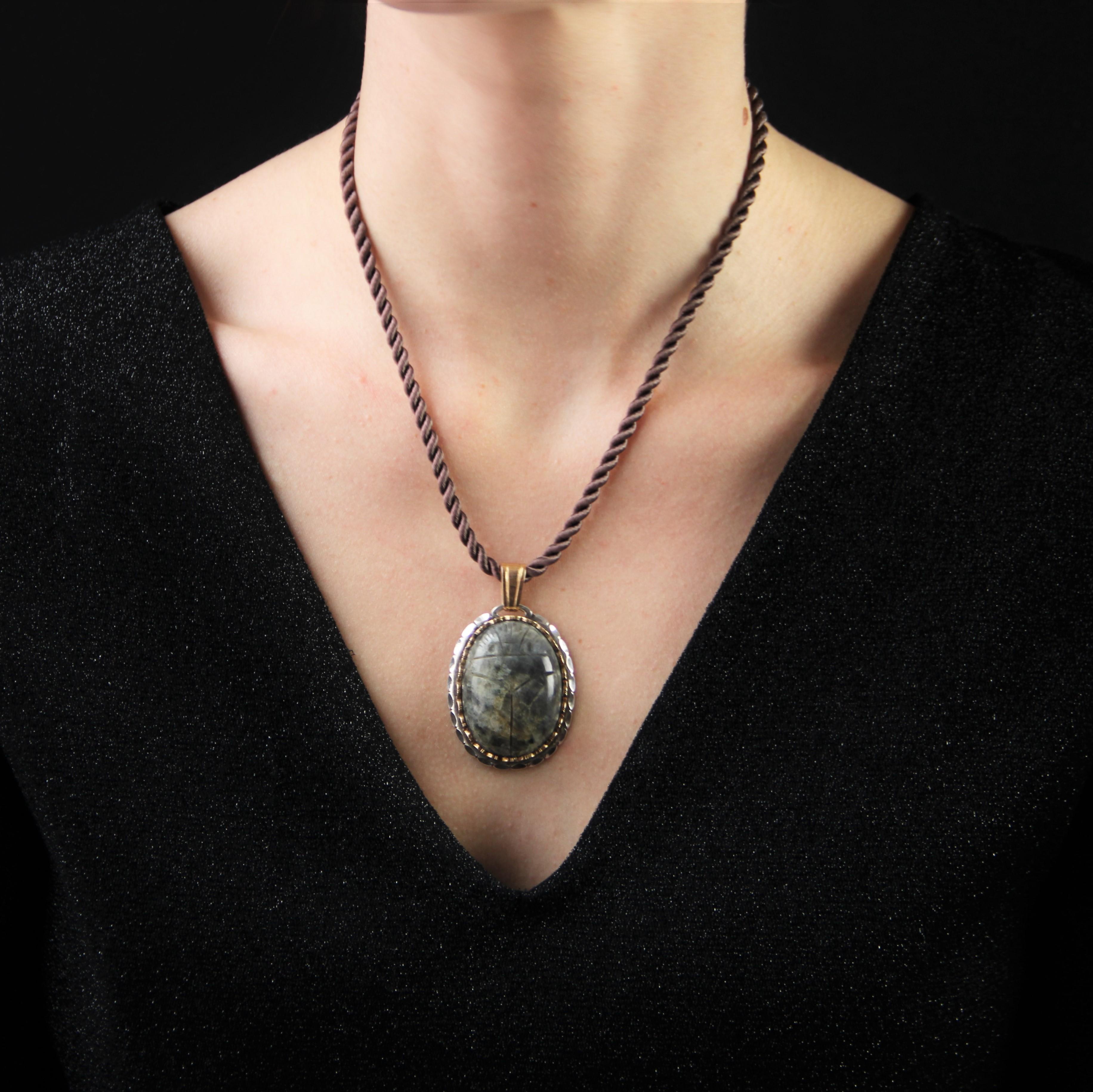 Silver and gold pendant.
Important oval shape pendant, it is set with a cabochon of labradorite engraved with a beetle pattern surrounded by a gold pattern such as a corolla, and a silver drape. The clasp is in yellow gold.
Height : 5,5 cm