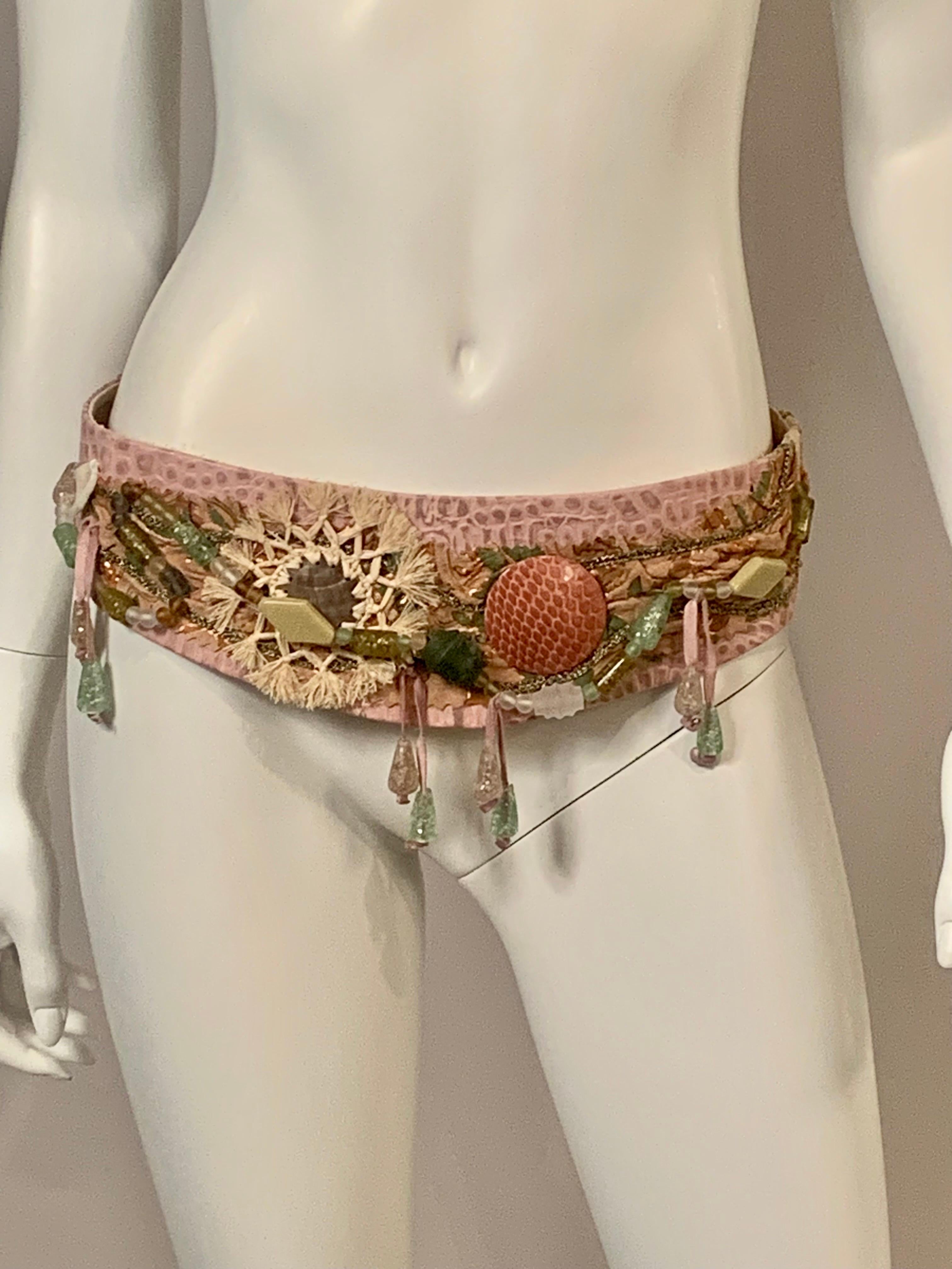 An amazing belt in the rich hippie style of the 1970's is made from pink faux alligator or  stamped leather and pink suede with a pink snakeskin disk and a shell and straw ornament.  In addition there are strands of glass beads, beads dangling from