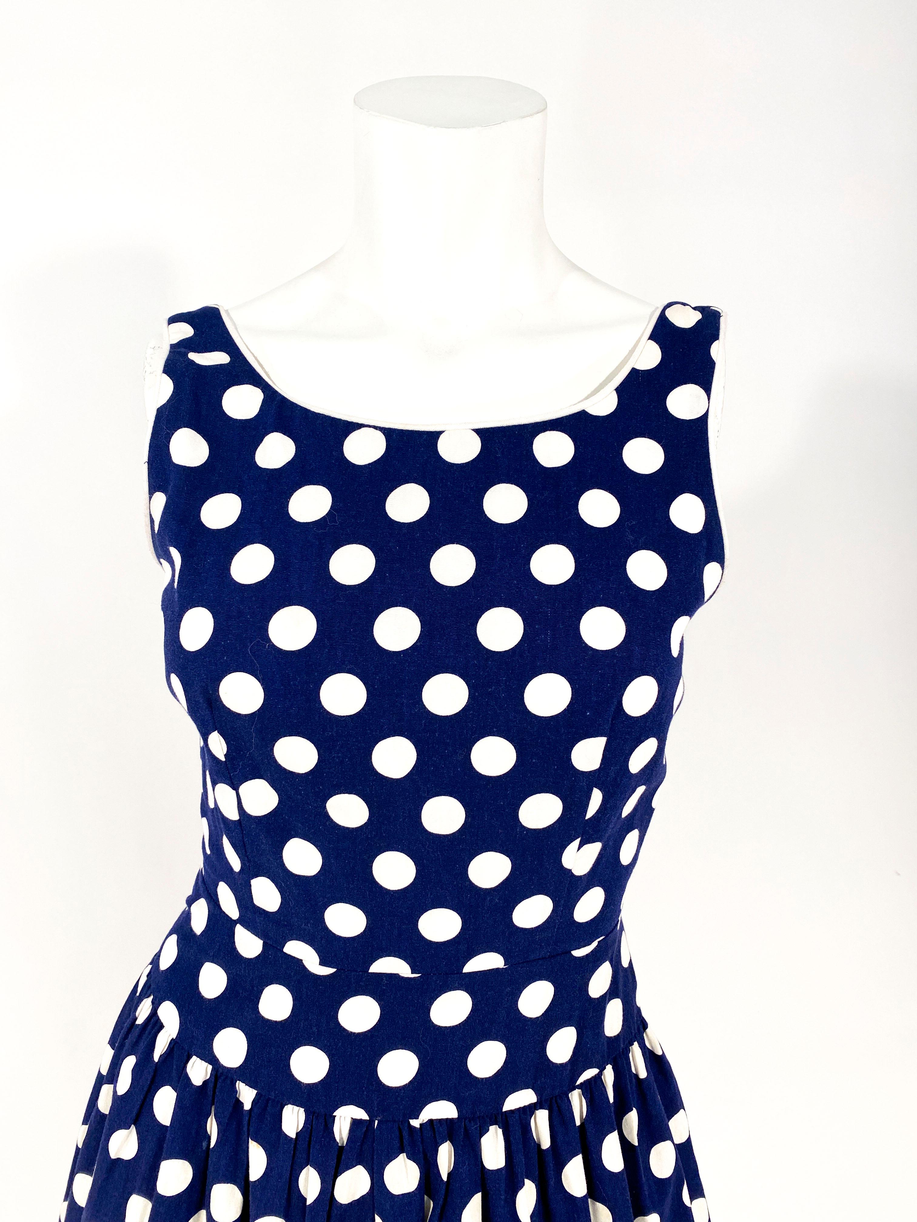 1960s Lanz navy blue cotton dress featuring bold white polka-dots, a drop waist line, in-set cummerbund, full tea length skirt, scoop neckline, low backline, and white contrasting piping along got neck and arms. This dress has been styled and