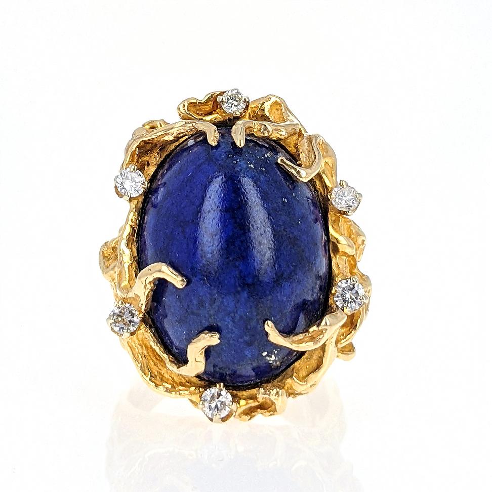 This 1970s bold statement ring centers upon an oval-shaped cabochon lapis lazuli accented by six round brilliant-cut diamonds and mounted in 14 karat yellow gold. It is size 5 with an inner ring guard. 
