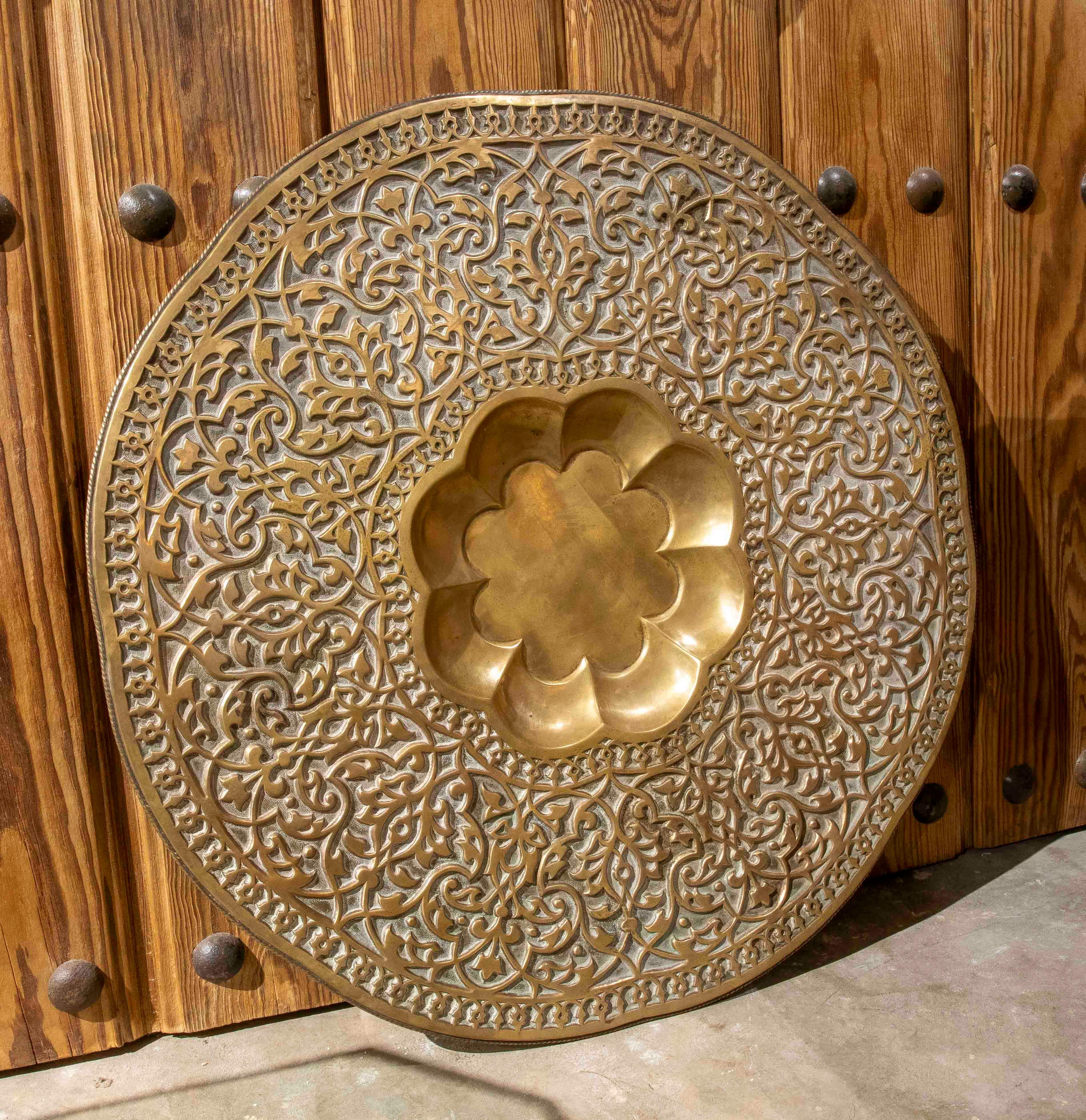 Espectacular bandeja antigua de latón repujado y calado, decorada con un elaborado motivo arabesco que cubre toda su superficie. En su centro hay una cavidad floral lobulada, característica de las piezas artesanales de influencia islámica.

La