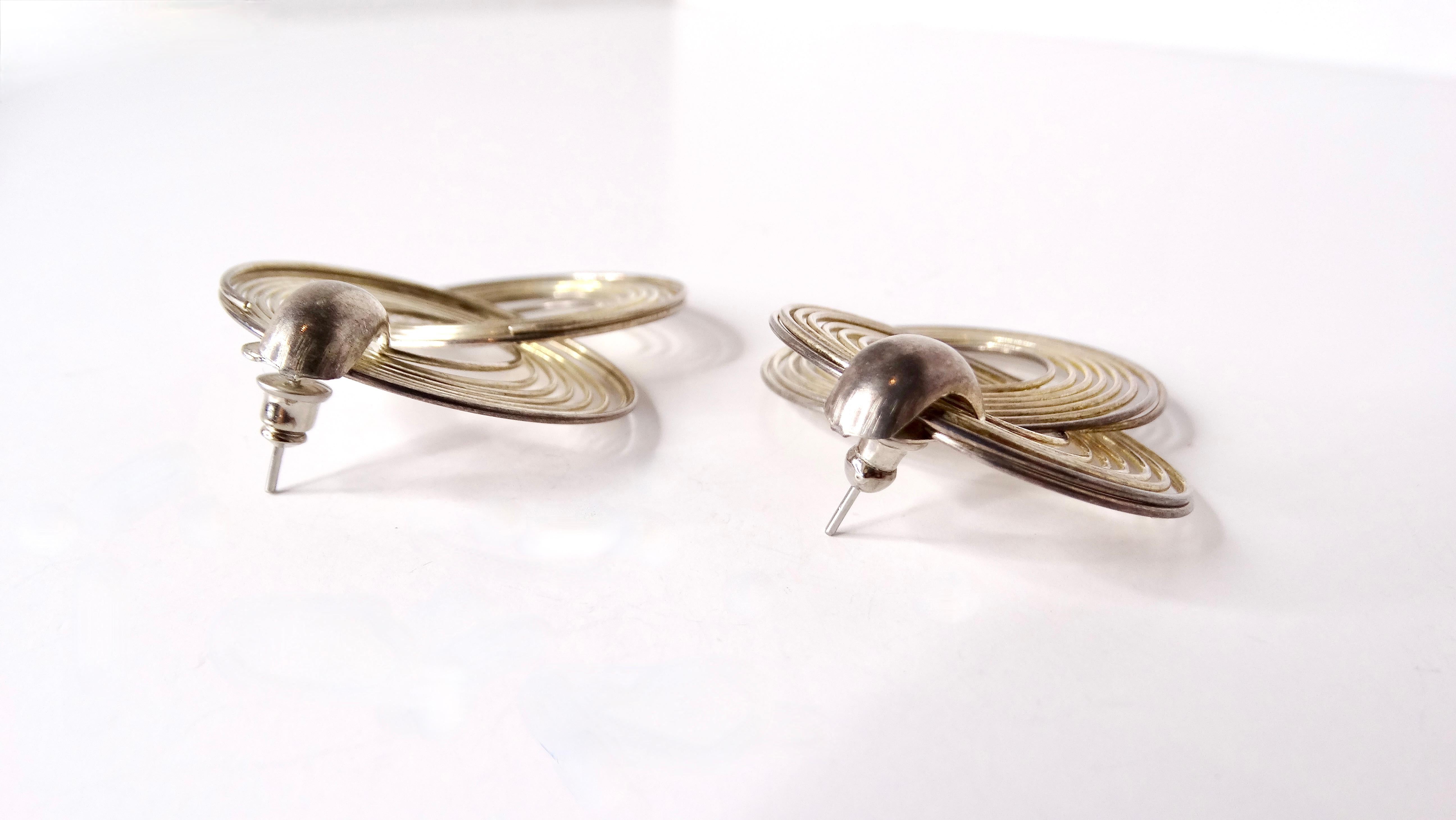 Entra nell'audace moda degli anni '70 con questi squisiti orecchini a cerchio grandi placcati in argento. Realizzati con un occhio di riguardo per l'estetica, questi orecchini presentano un accattivante design a orbita che penzola giocosamente,