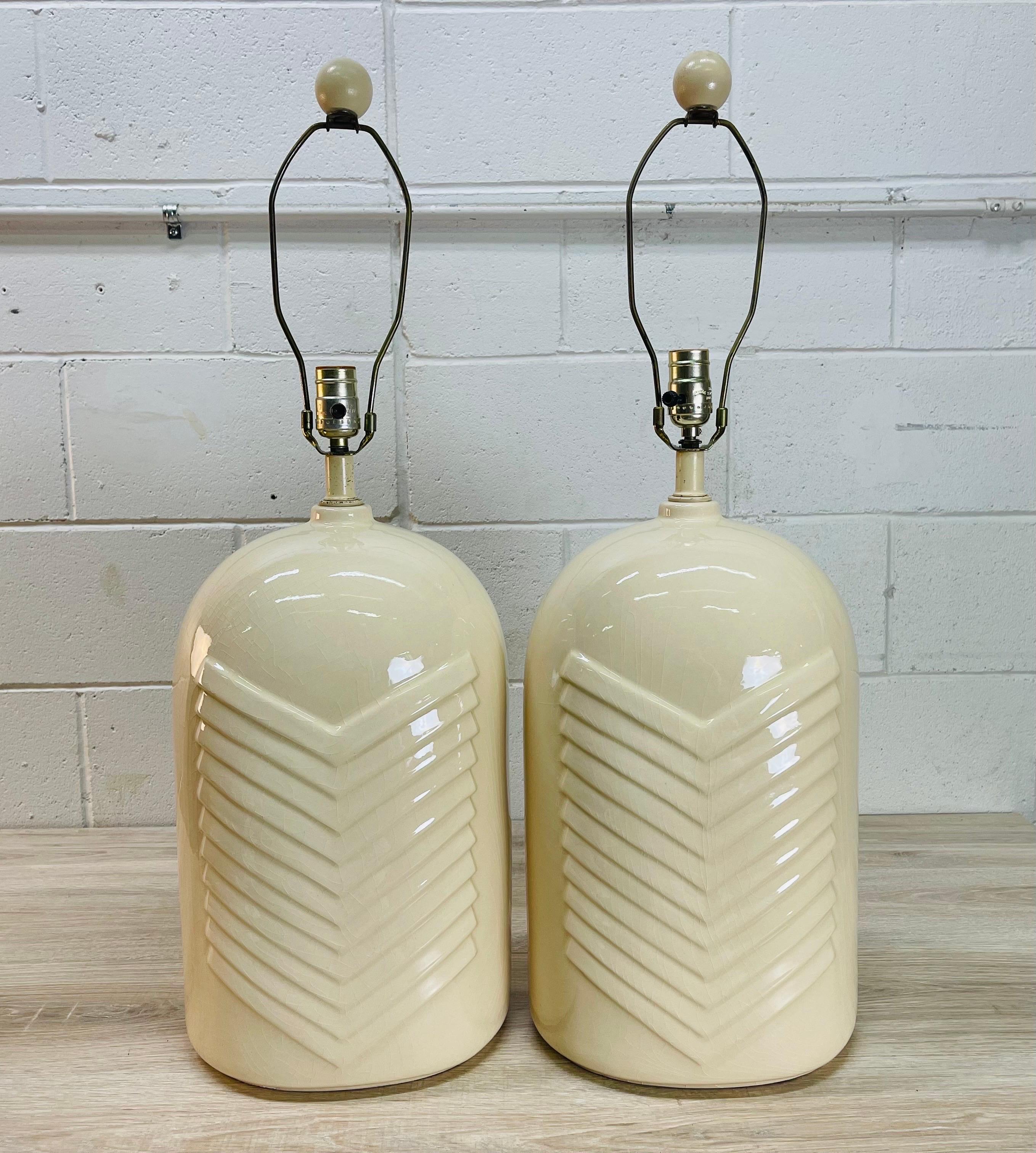 Vintage 1970s pair of white ceramic table lamps with a chevron design. The lamps also have a craze in the glaze all over the lamps and is part of the design. Both lamps come with round ball wood finials. Wired for the US and in working condition.