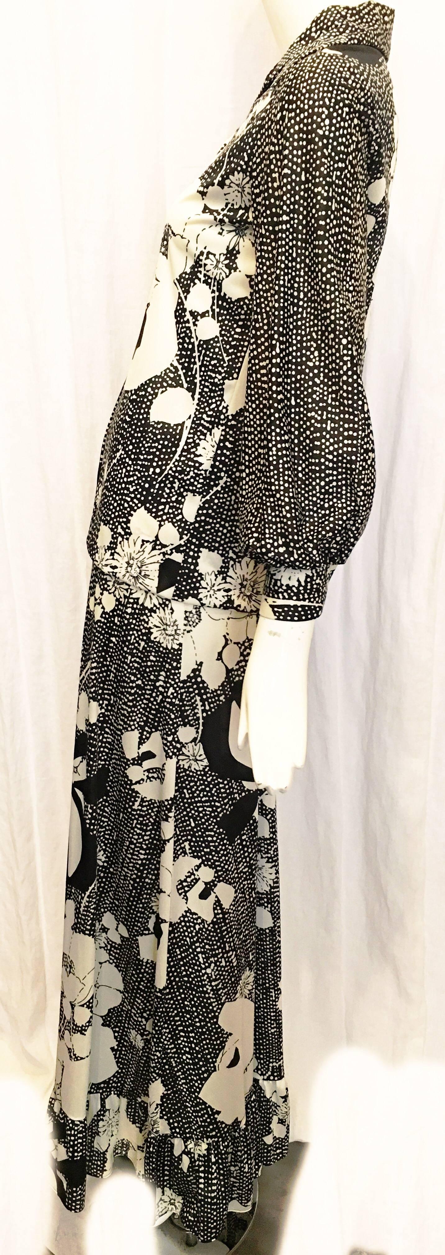 White and black floral skirt suit in the style of Hawaiian textiles. Top is button down with five buttons down the front and a single button at each cuff of the sleeves. Hem is hand sewn. Skirt is full length with ruffle trim and elastic at the
