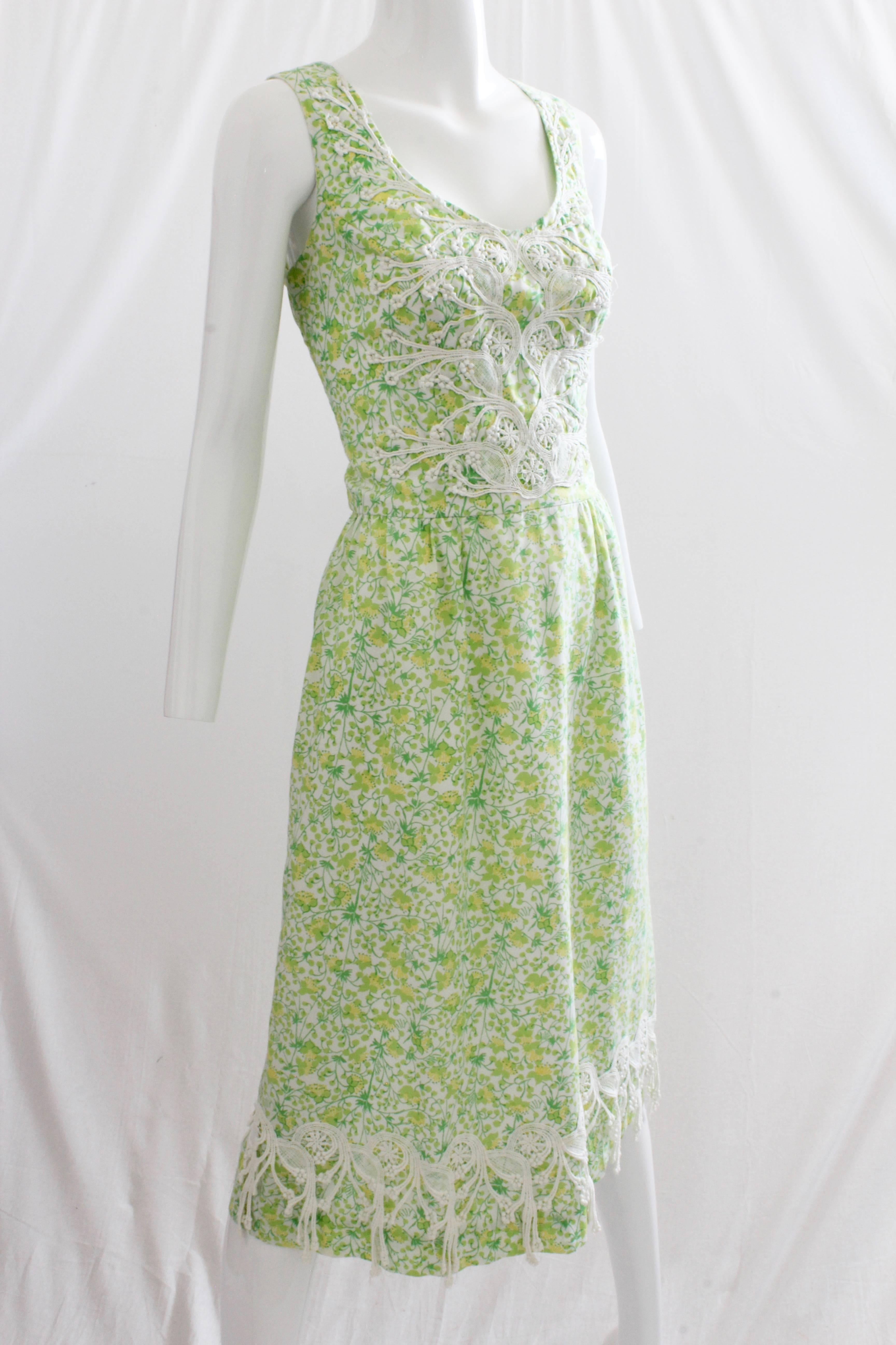 This lovely dress was made by Lilly Pulitzer, most likely in the early 1970s. Made from cotton floral print fabric in shades of green, yellow and white, this dress features a cinched waist, a white lace-covered bodice and a white lace hanging trim